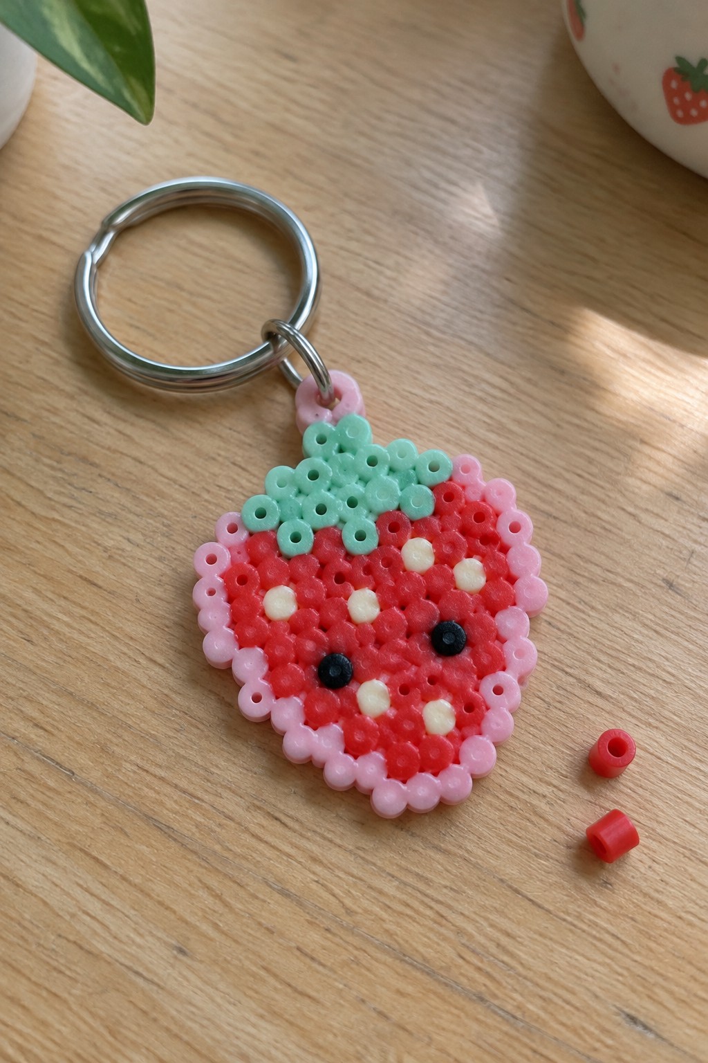 Perler bead strawberry keychain with pink border, green leaves, and cute face