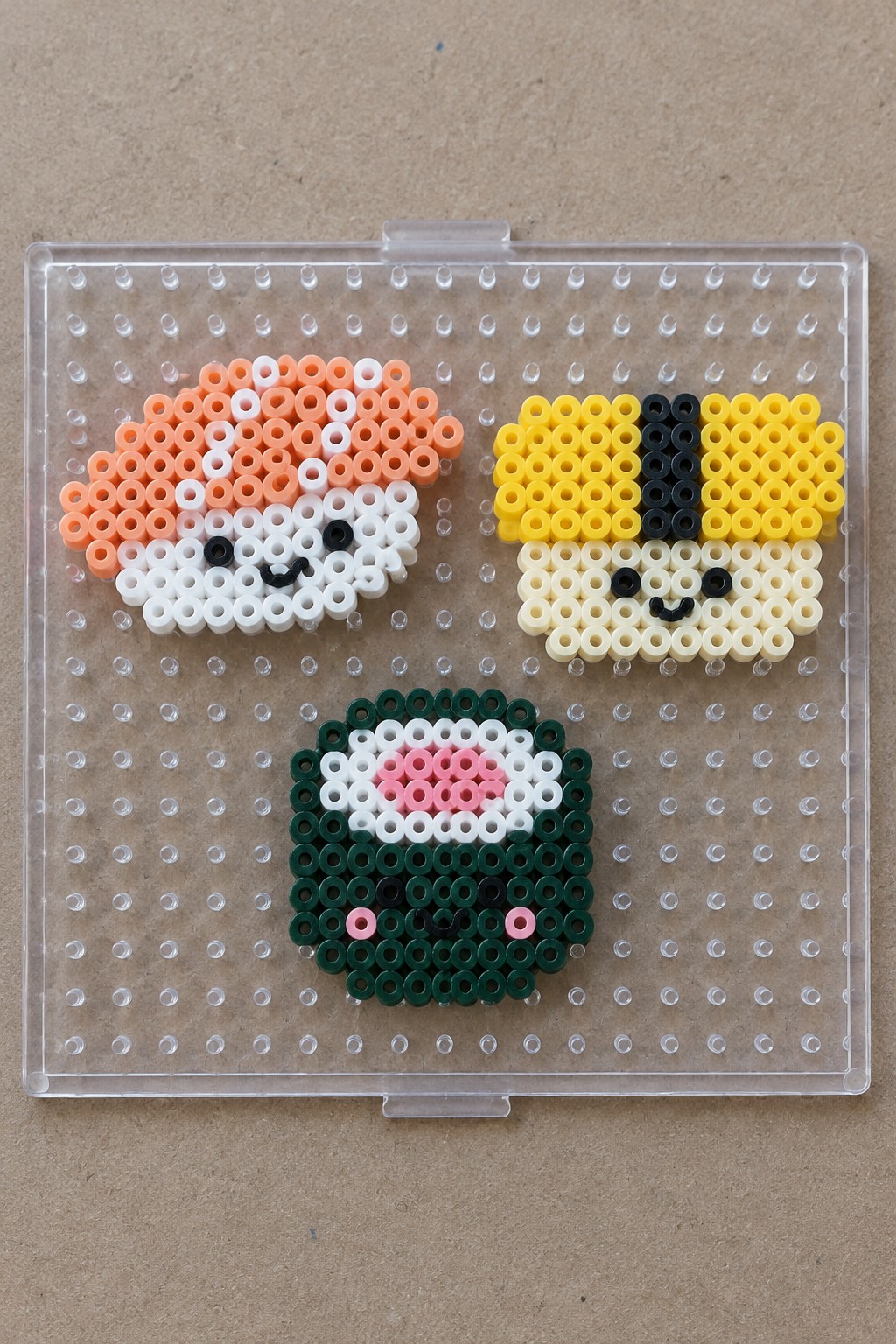 Three perler bead animal faces in orange, yellow, and green on pegboard.