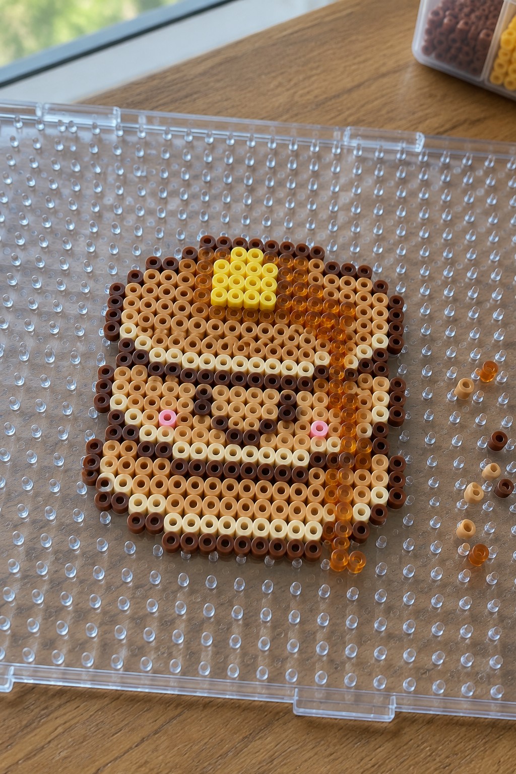 Perler beads forming a chocolate chip cookie with pink cheeks on pegboard