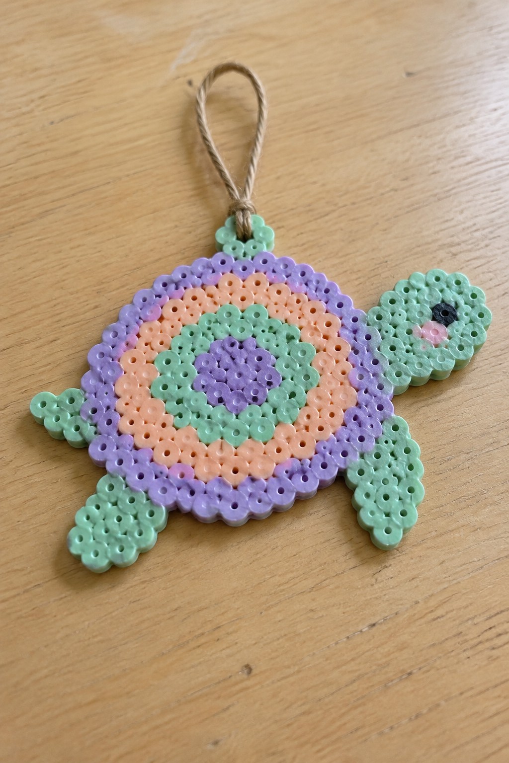 Colorful perler bead turtle with concentric pastel shell and twine hanging loop.