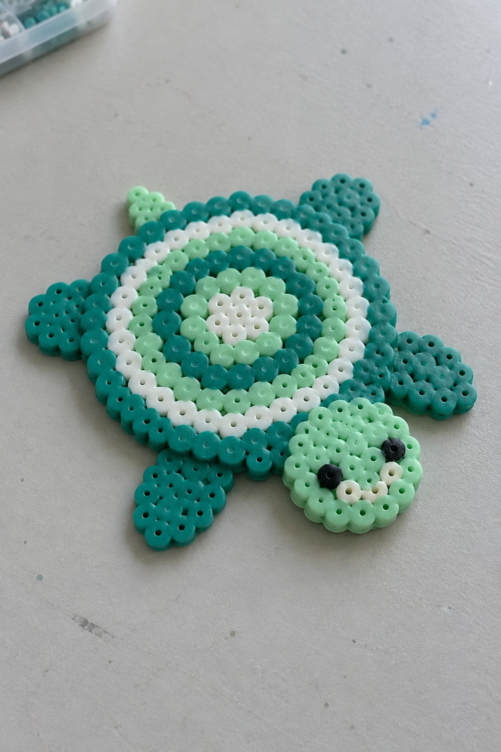 Perler bead turtle with concentric shell rings in teal, green, and white on a pegboard.