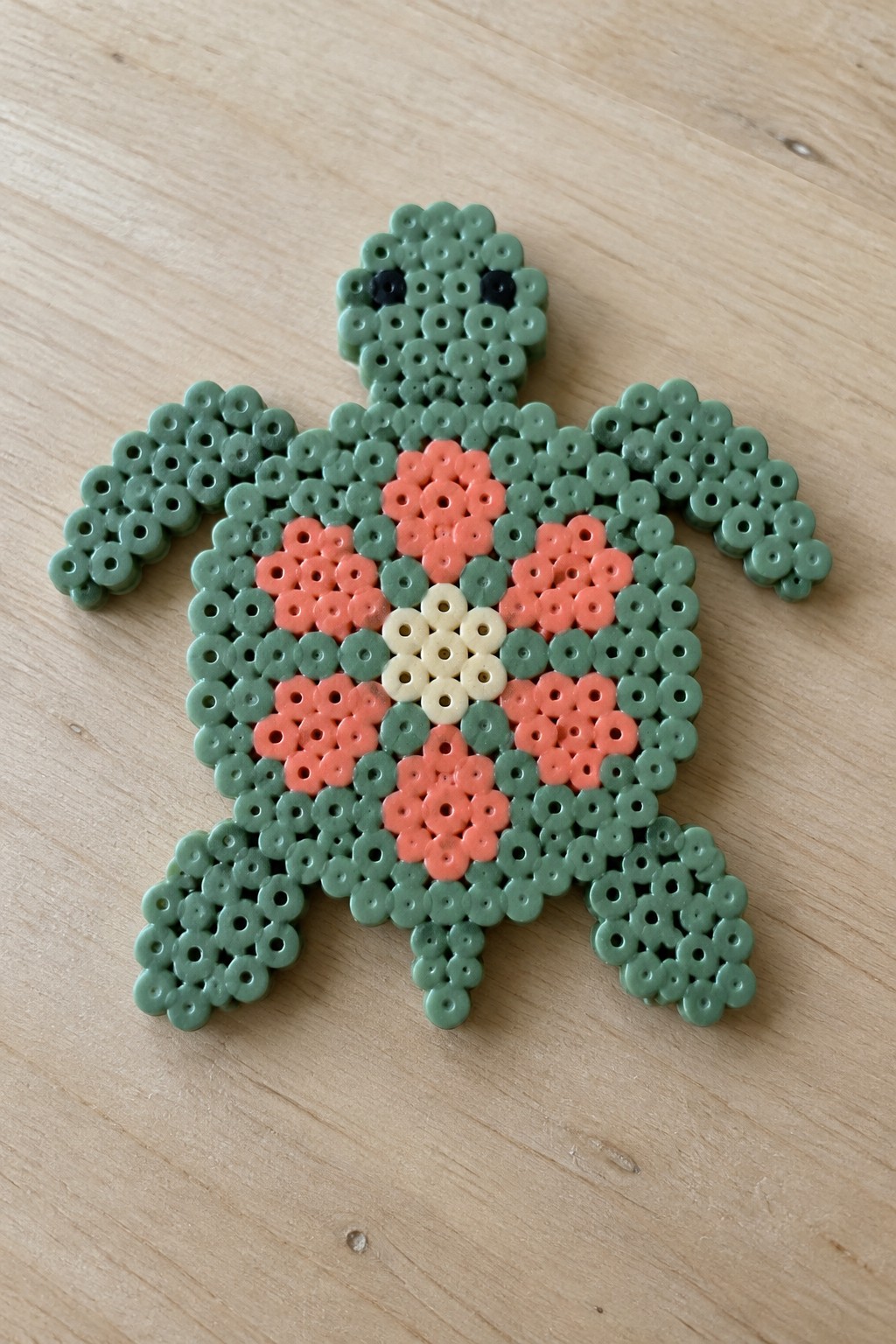 Green perler bead turtle with pink floral shell on wooden surface