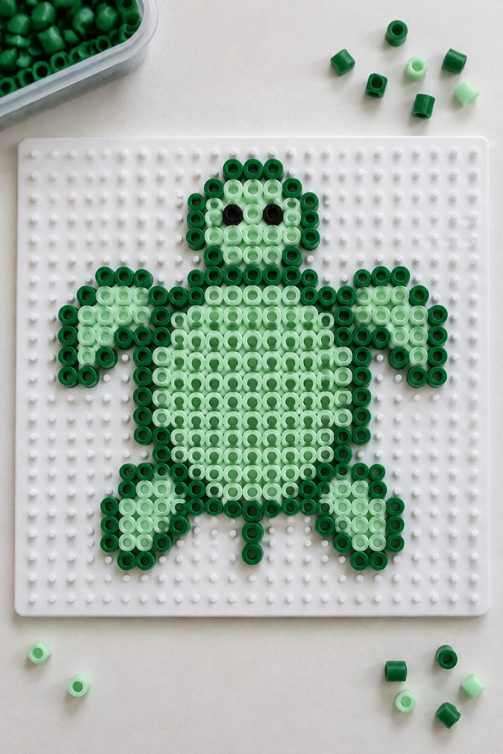 Green turtle Perler bead pattern on a pegboard using several shades of green with black bead eyes.