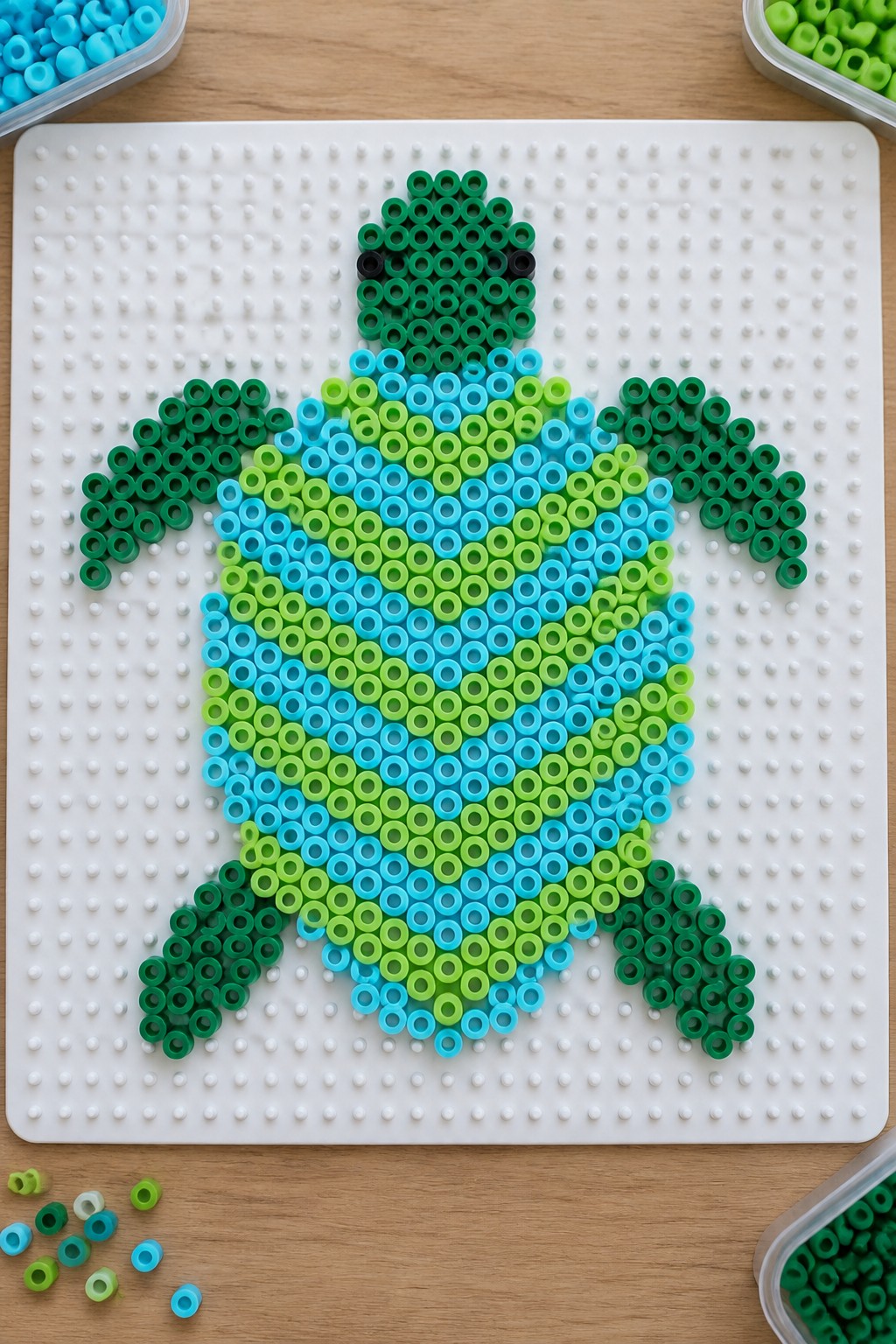 Gradient green-blue sea turtle perler bead art on white pegboard with loose beads nearby