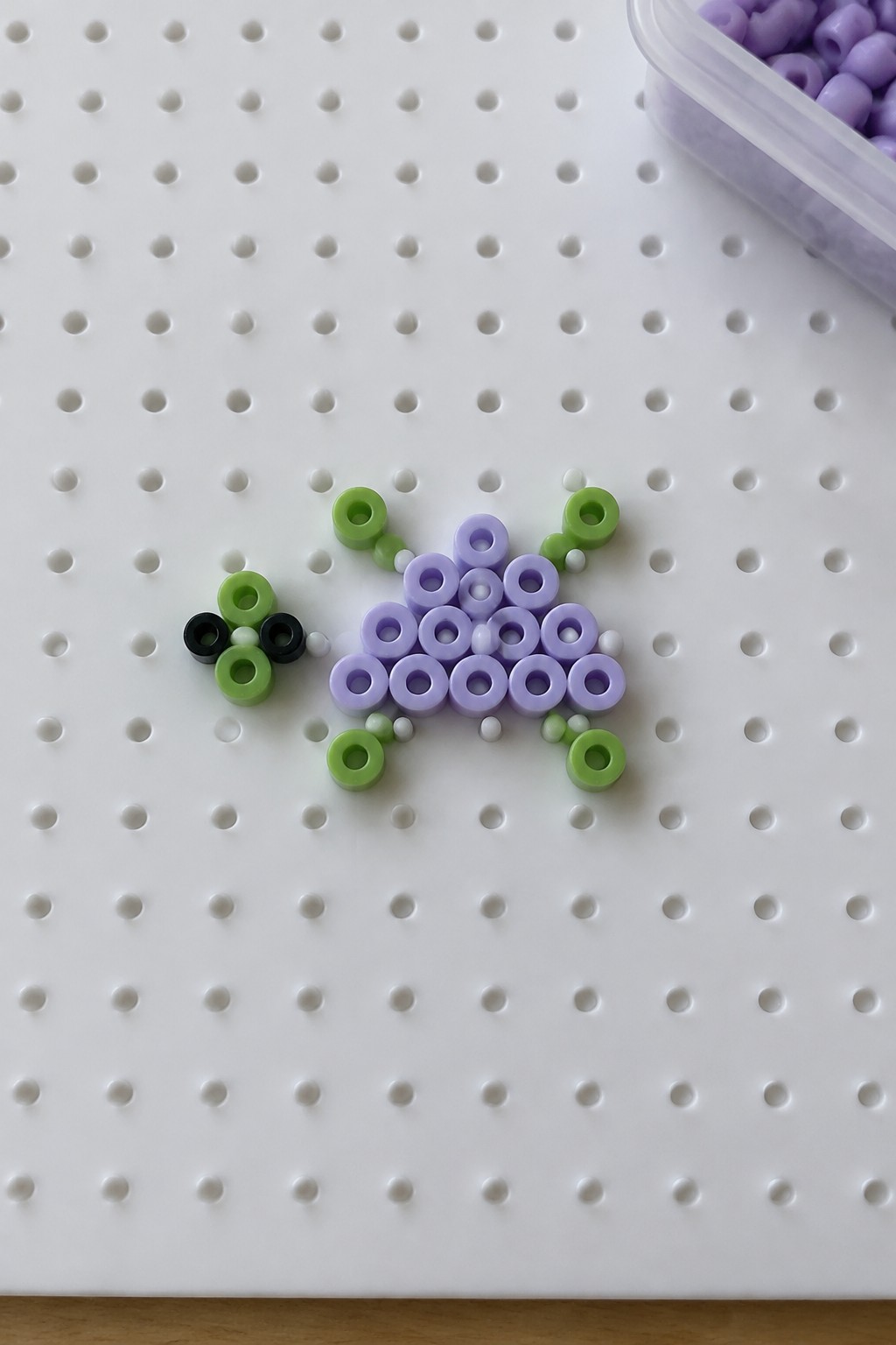 Perler bead turtle with purple shell and green limbs on a white pegboard.