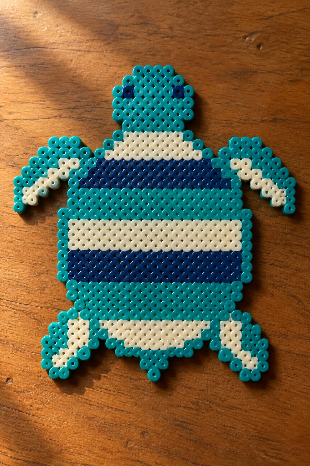 Turquoise perler bead turtle with navy striped shell on wood