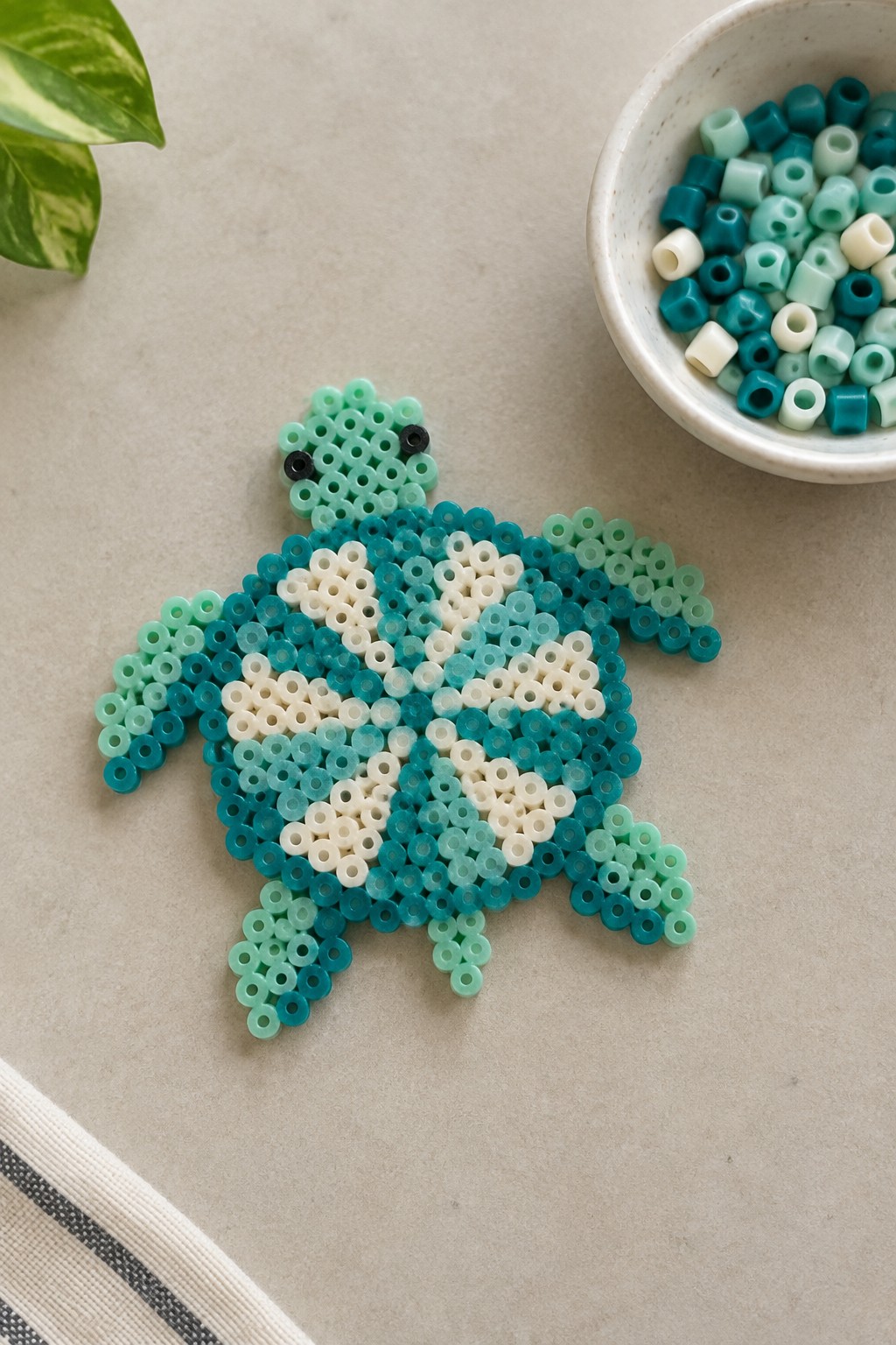 Sea turtle perler bead craft in teal tones beside bowl of beads
