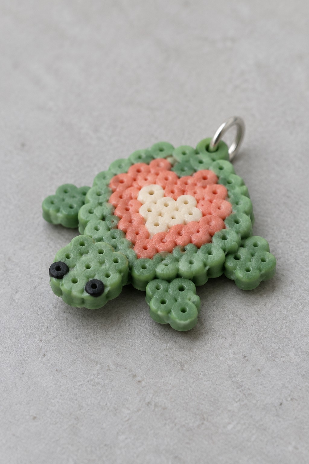 Fused Perler bead turtle with green body and coral-cream heart pattern on shell, metal ring attached at top.