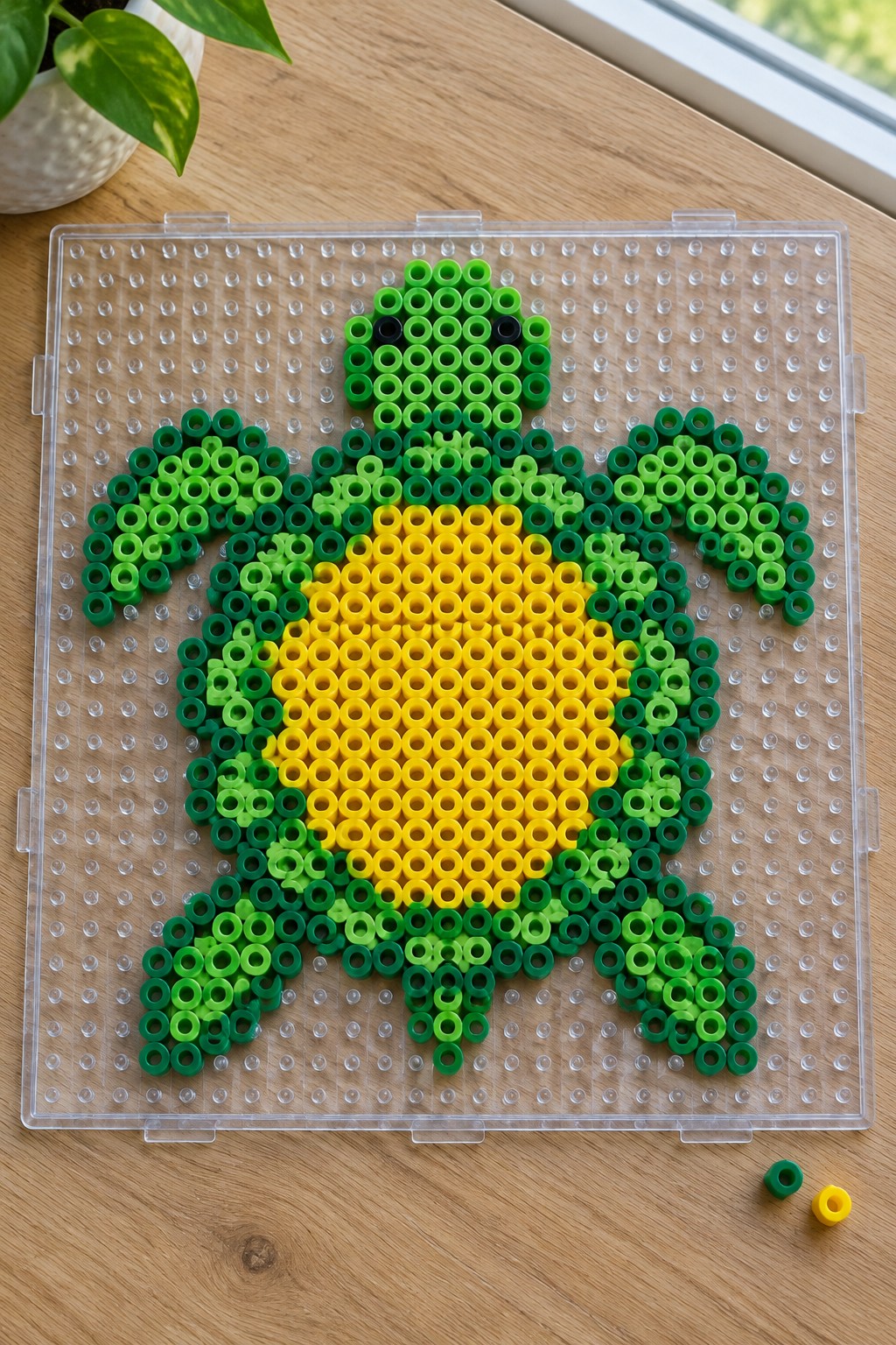 Green and yellow perler bead turtle on clear pegboard over wooden table