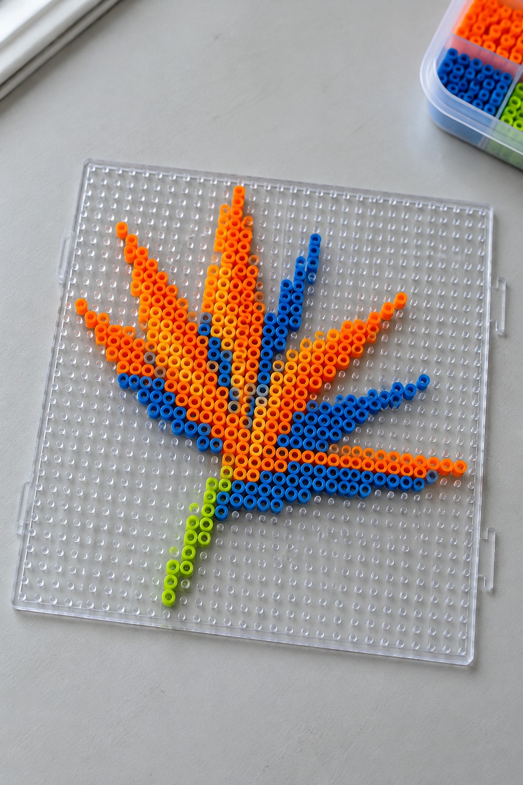Colorful perler beads forming a cannabis leaf on a clear pegboard with extra beads nearby.