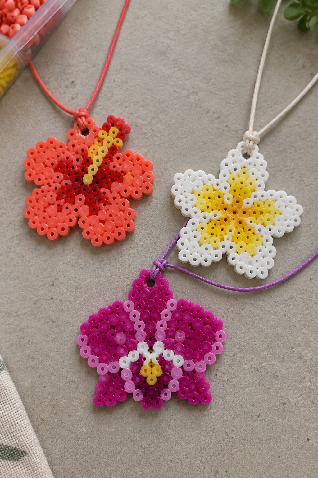 Three colorful perler bead flower necklaces on red, white, and purple cords.