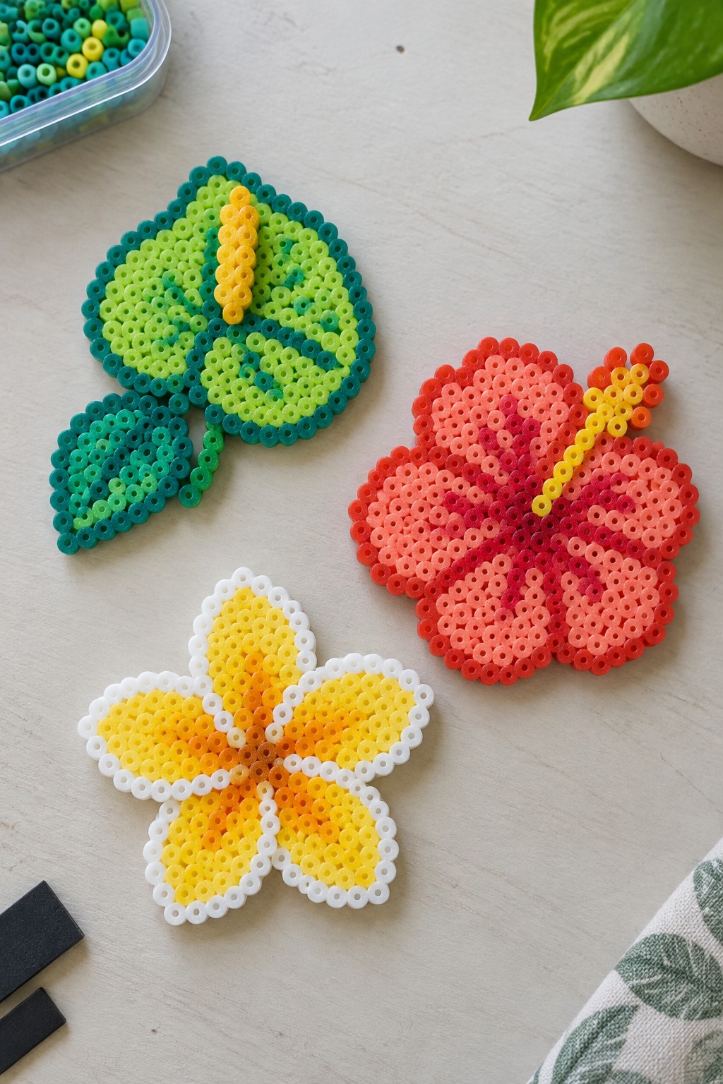 Perler bead crafts of green leaf, yellow flower, and red hibiscus on table