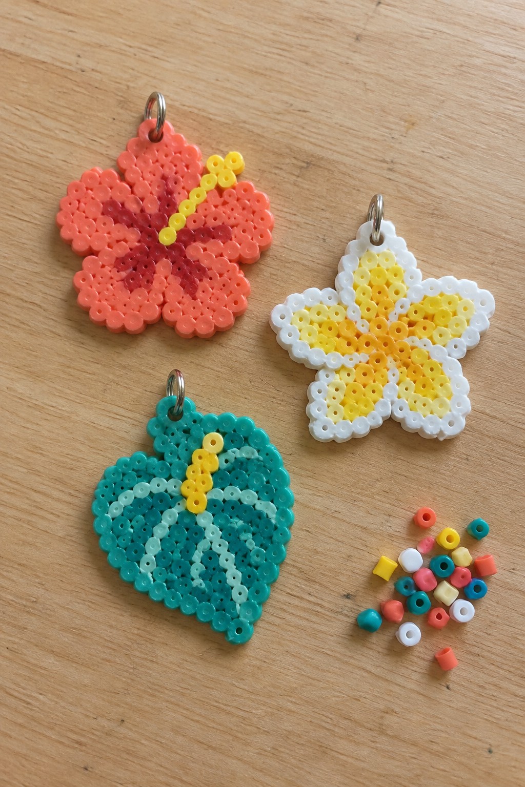 Pink flower, yellow star, and teal leaf perler bead crafts with loose beads on wood.
