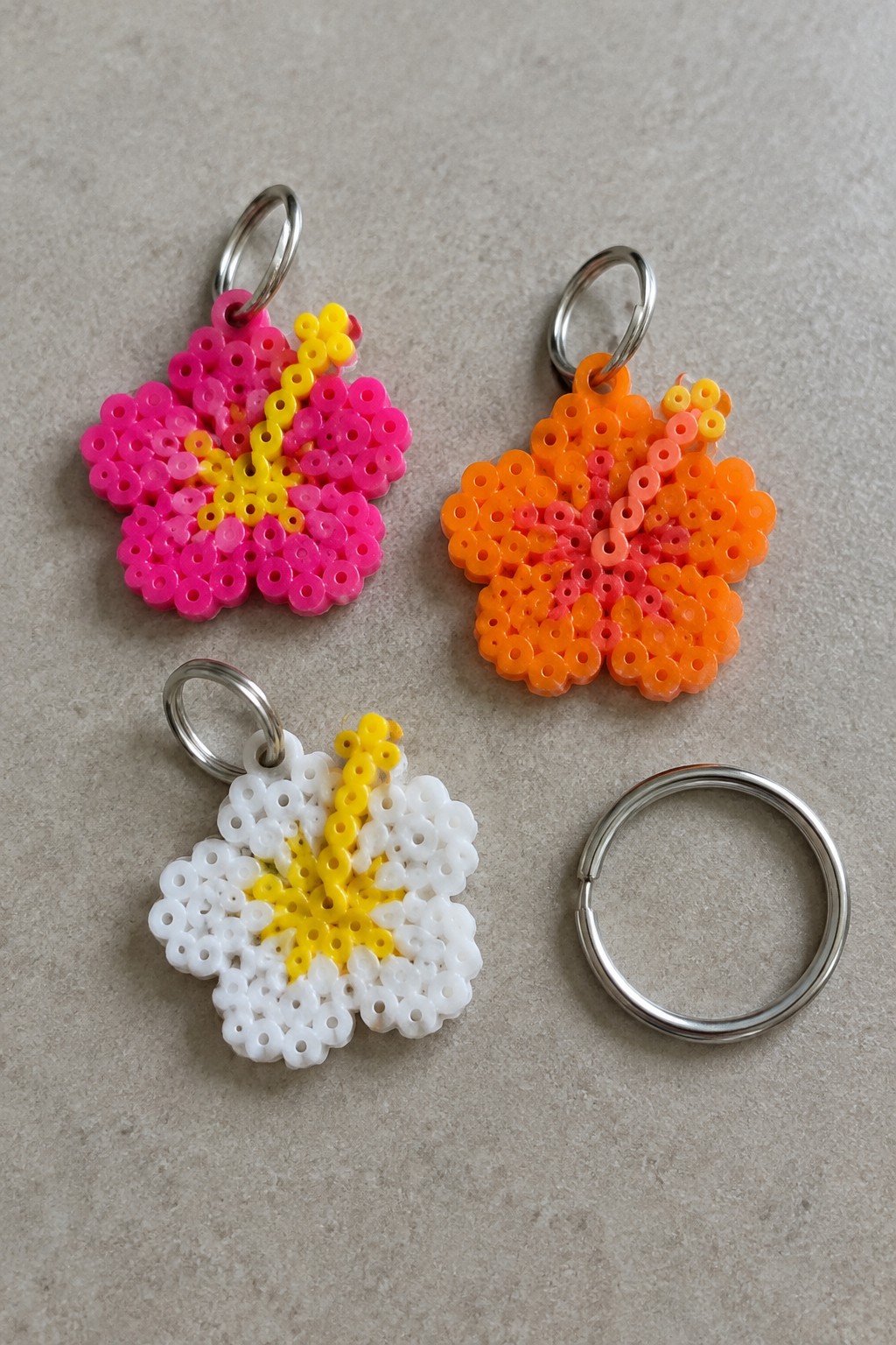 Three colorful perler bead flower keychains and one loose metal ring on gray surface.