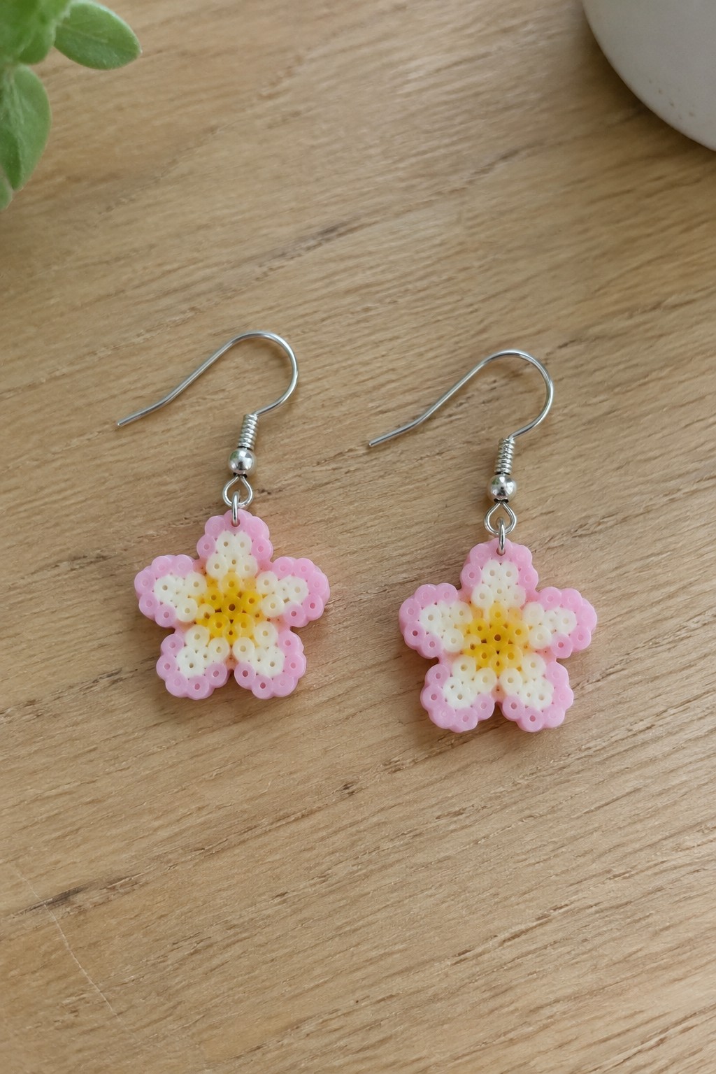 Two fused Perler bead flower earrings in pink, white, and yellow with metal hooks.