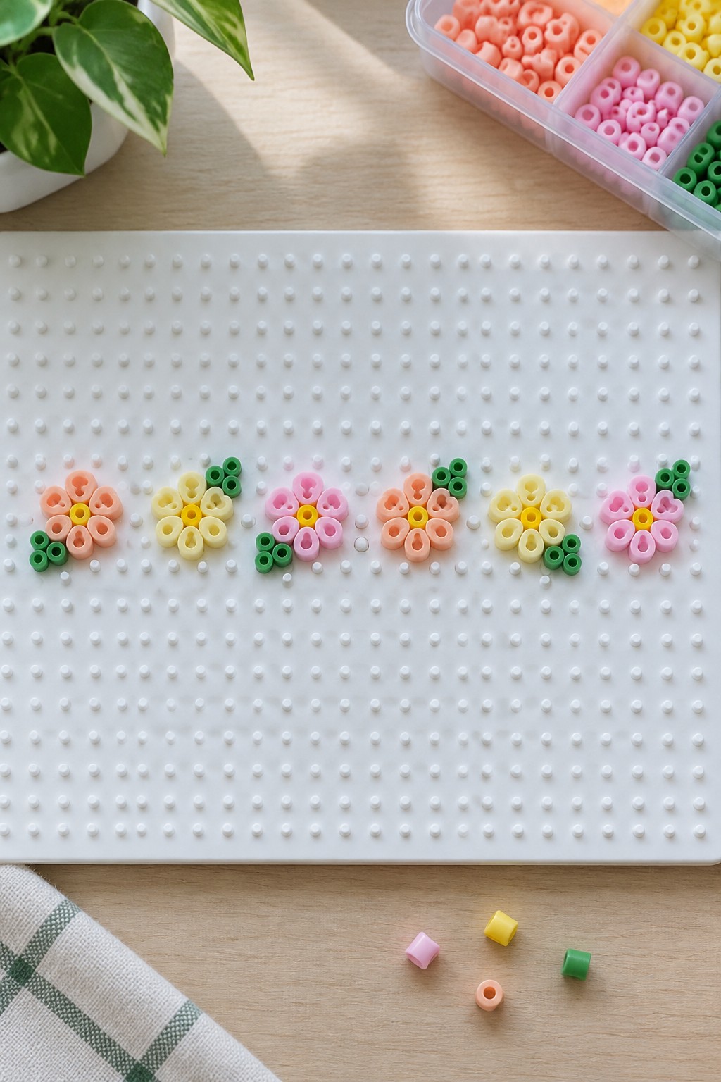 Colorful perler bead flowers lined up on a white pegboard with supplies nearby.