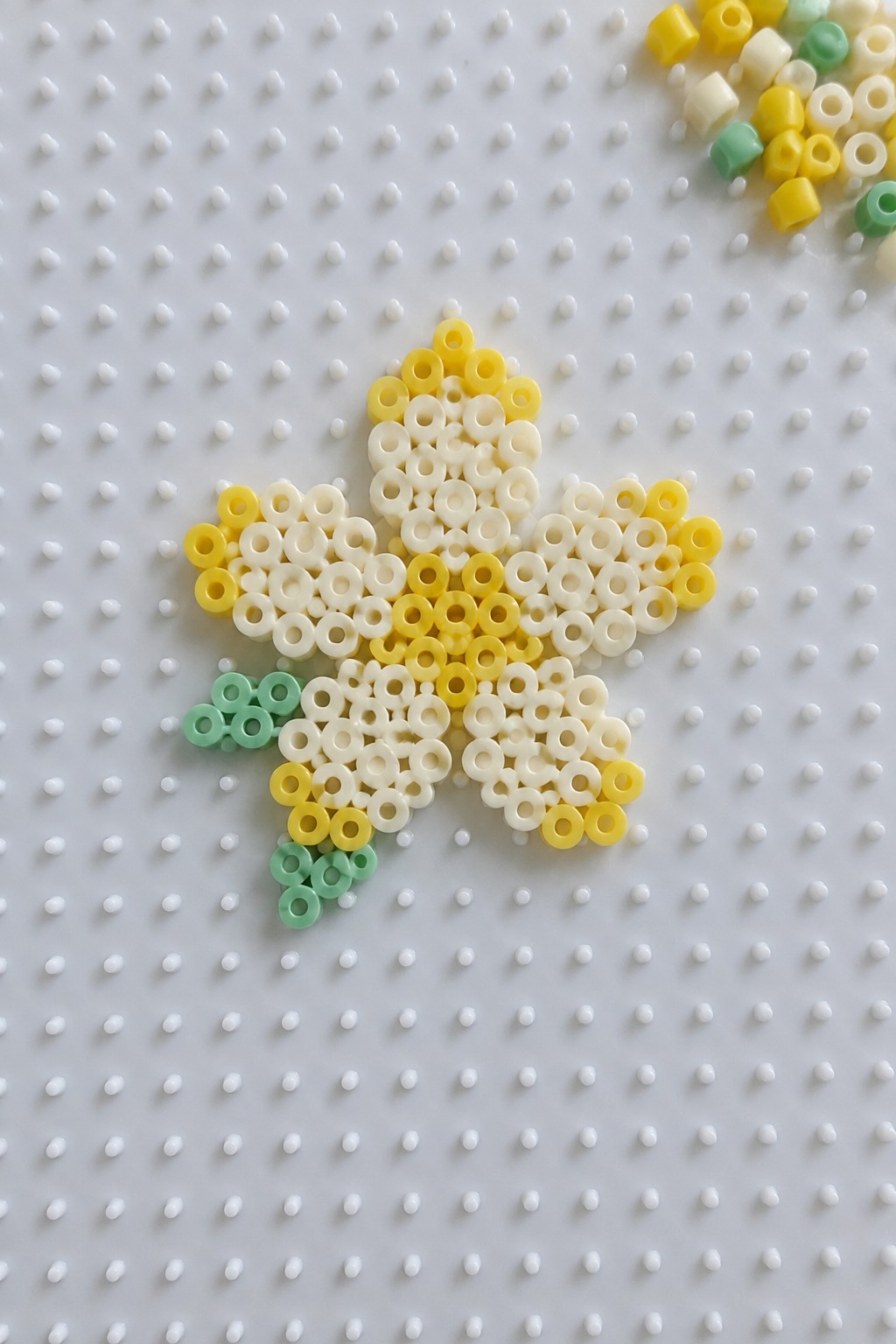 Yellow and white perler bead flower with green accents on pegboard