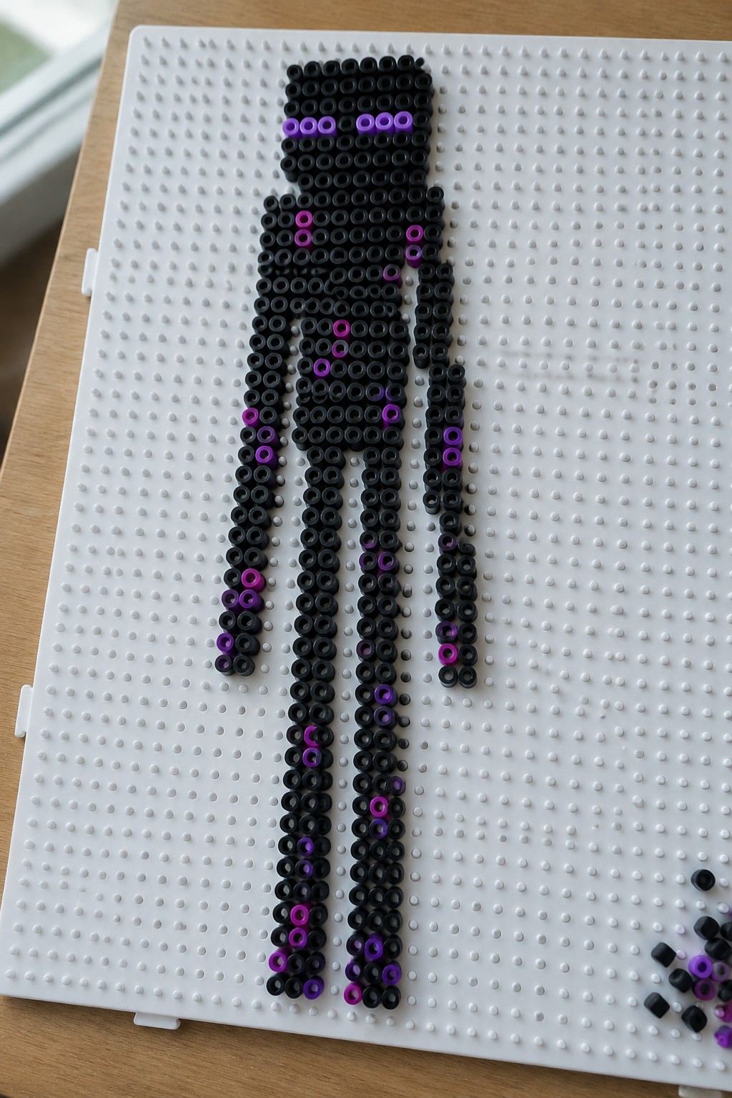 Black and purple beads forming a figure on white pegboard.