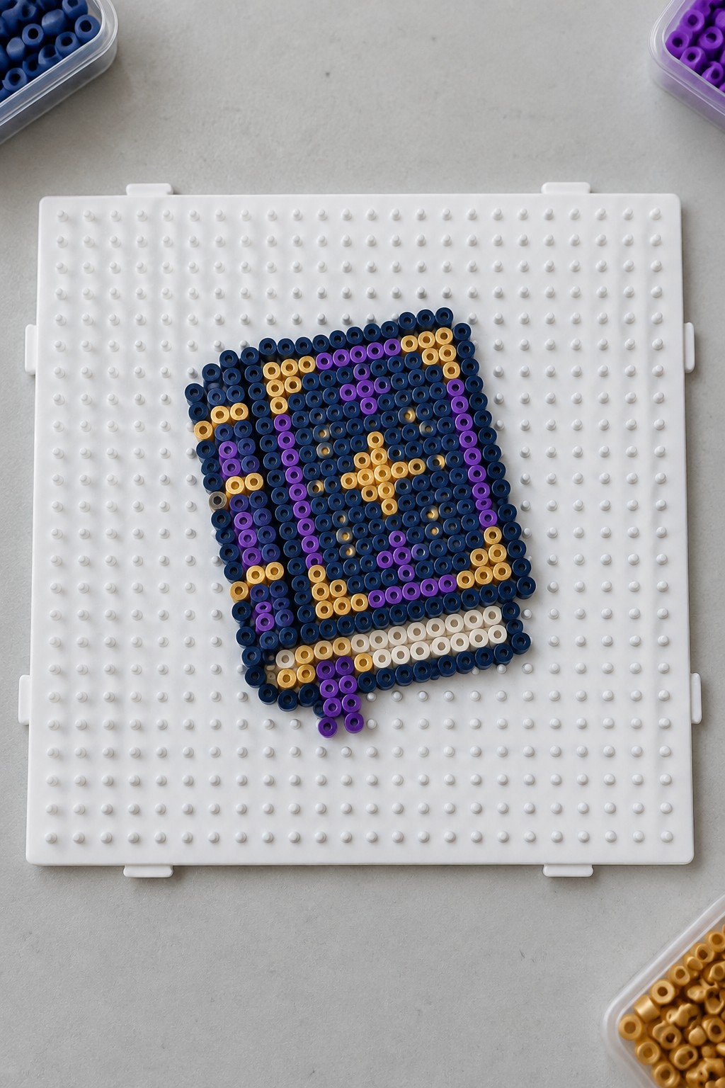 Unfused Perler beads on a pegboard forming a Minecraft chest design with navy blue, purple, yellow, and white beads.