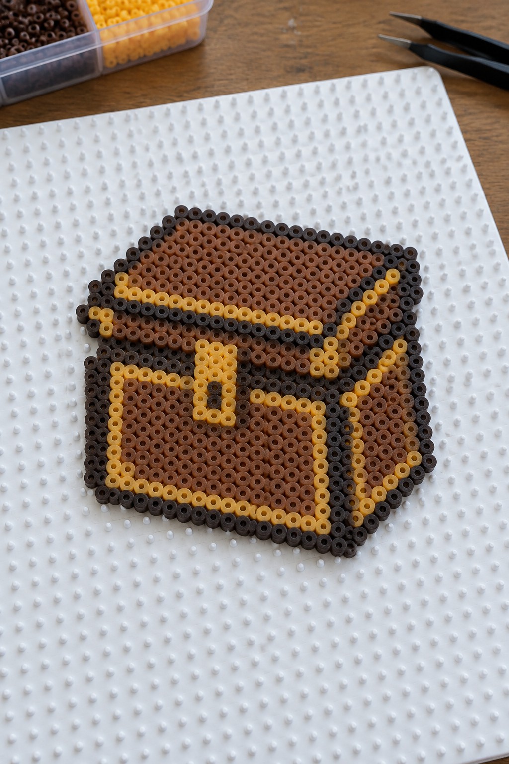 Perler beads forming brown and yellow chest design on white pegboard with tools nearby.