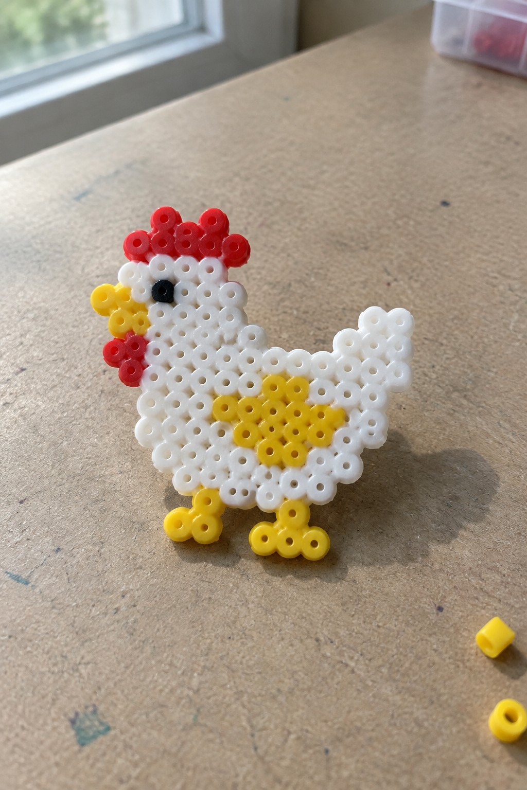 Perler bead chicken with white body, red comb, yellow beak and legs