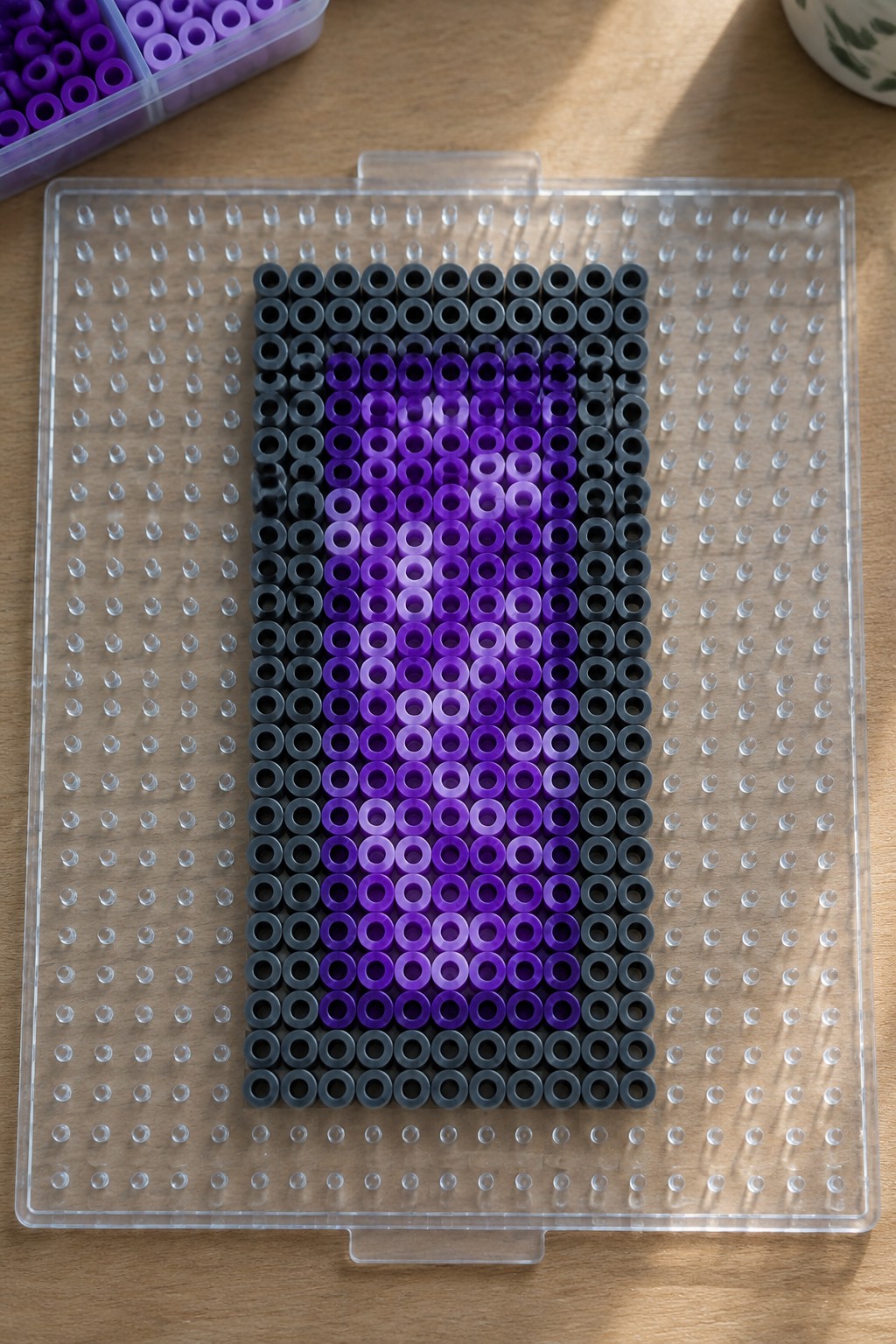 Perler beads on a pegboard forming a purple gradient heart with black borders.