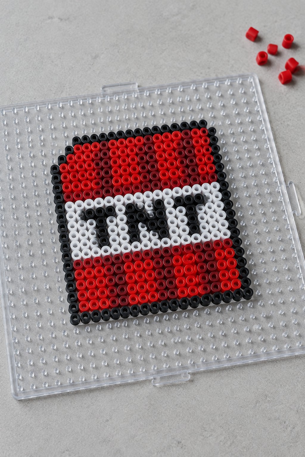 Perler bead creeper face pattern on a pegboard using black, red, and white beads.