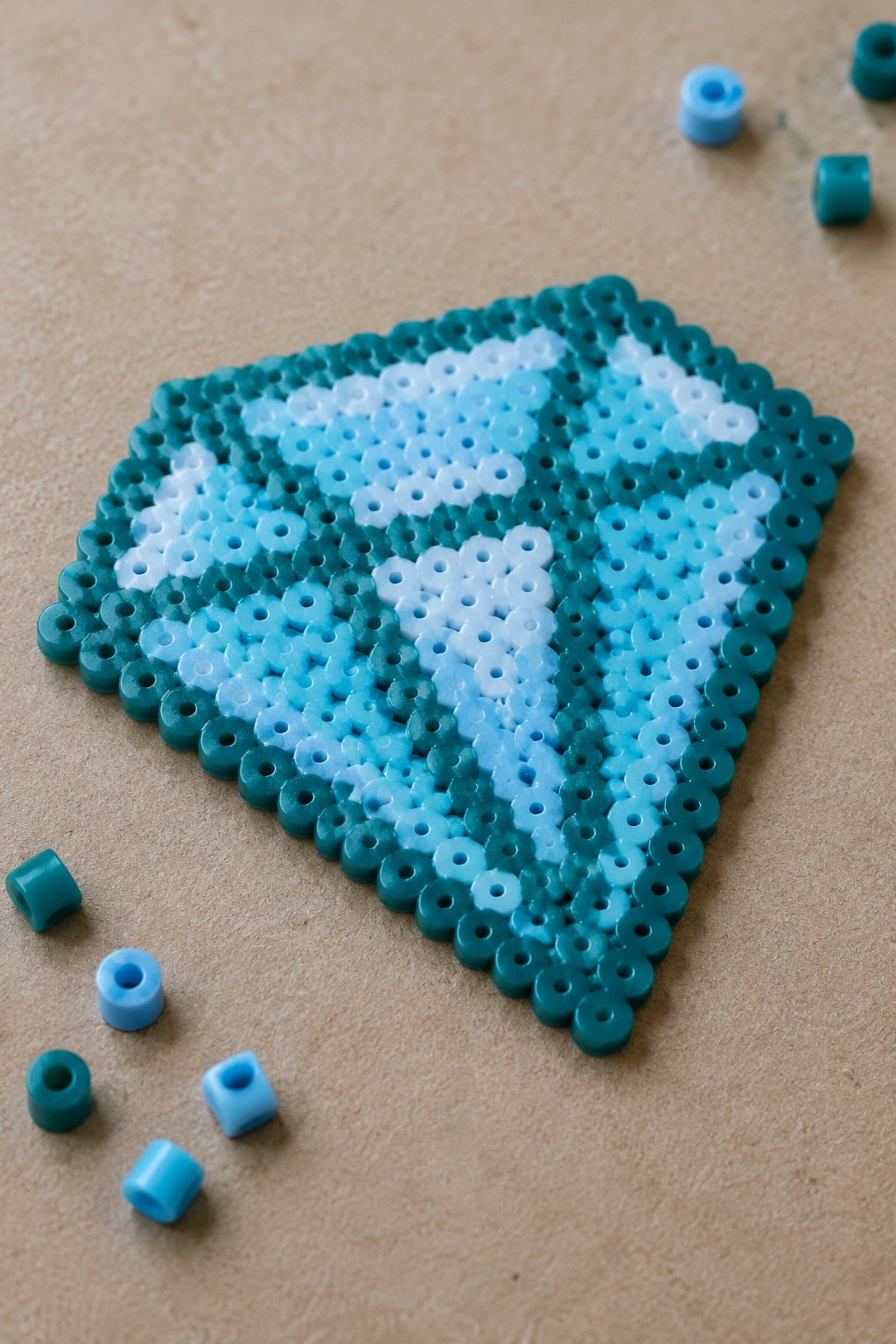 Triangular Perler bead art in blue and teal shades with loose beads on brown surface