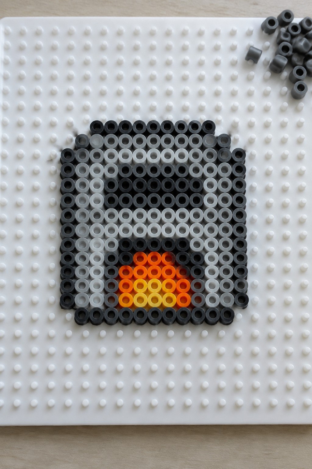 Black gray orange yellow perler beads forming pixel art square on white pegboard