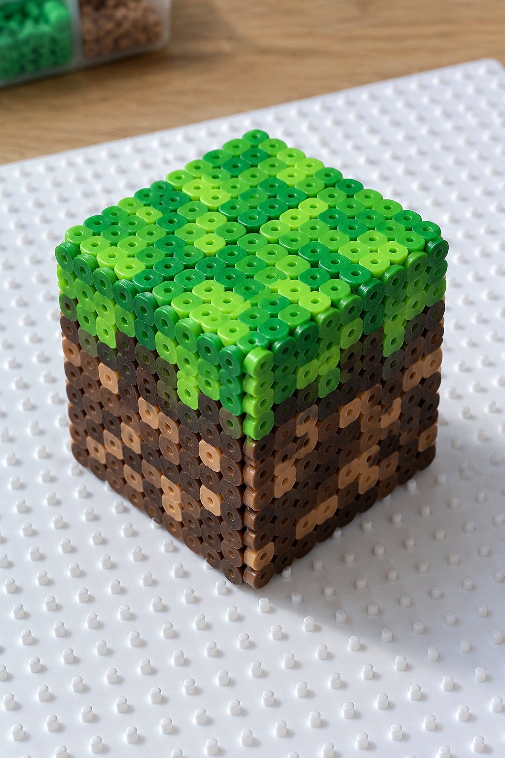 Minecraft grass block made from green and brown perler beads on pegboard.