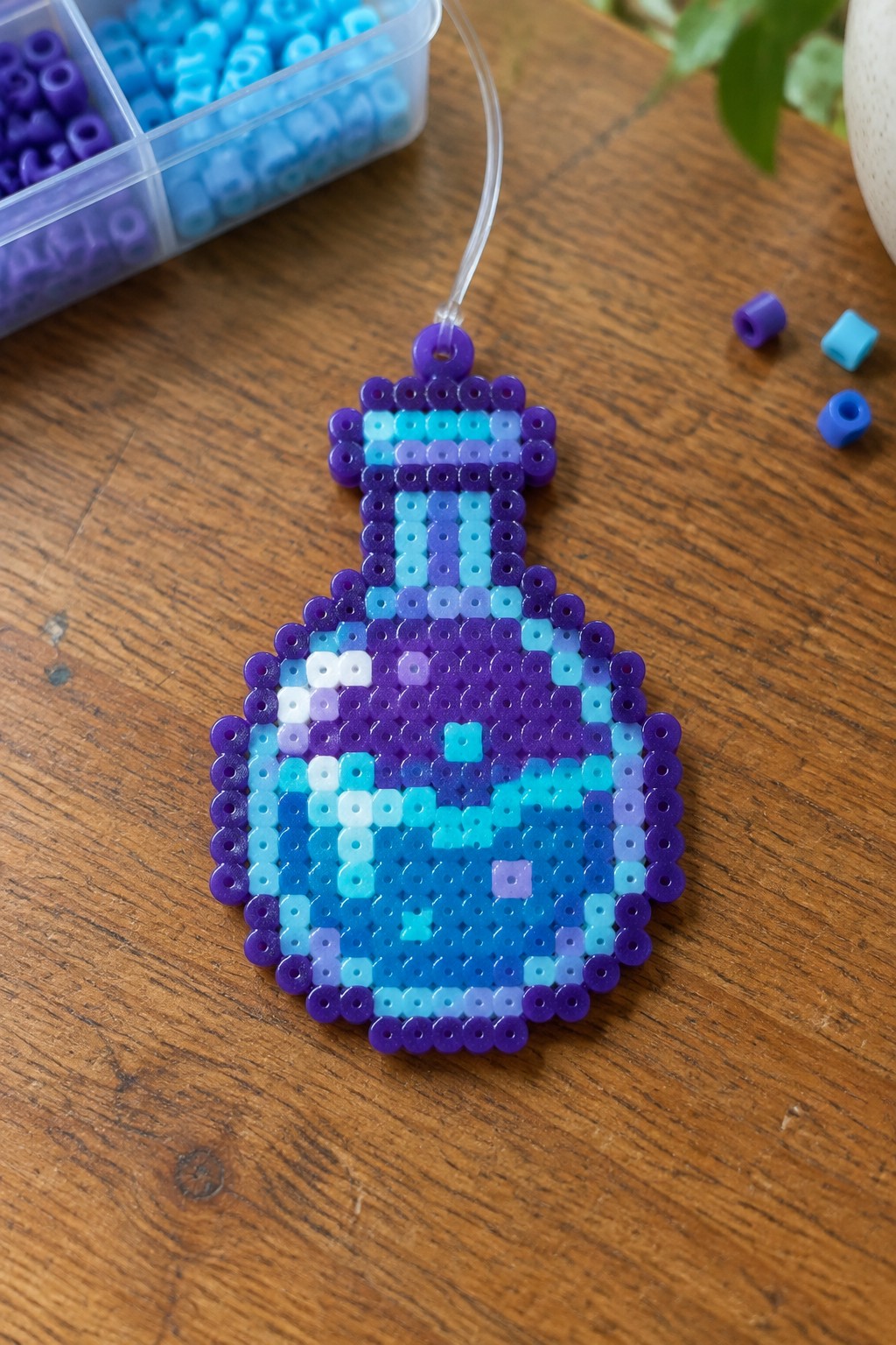 A Perler bead arrangement of a Minecraft potion bottle on a pegboard using purple and blue beads.