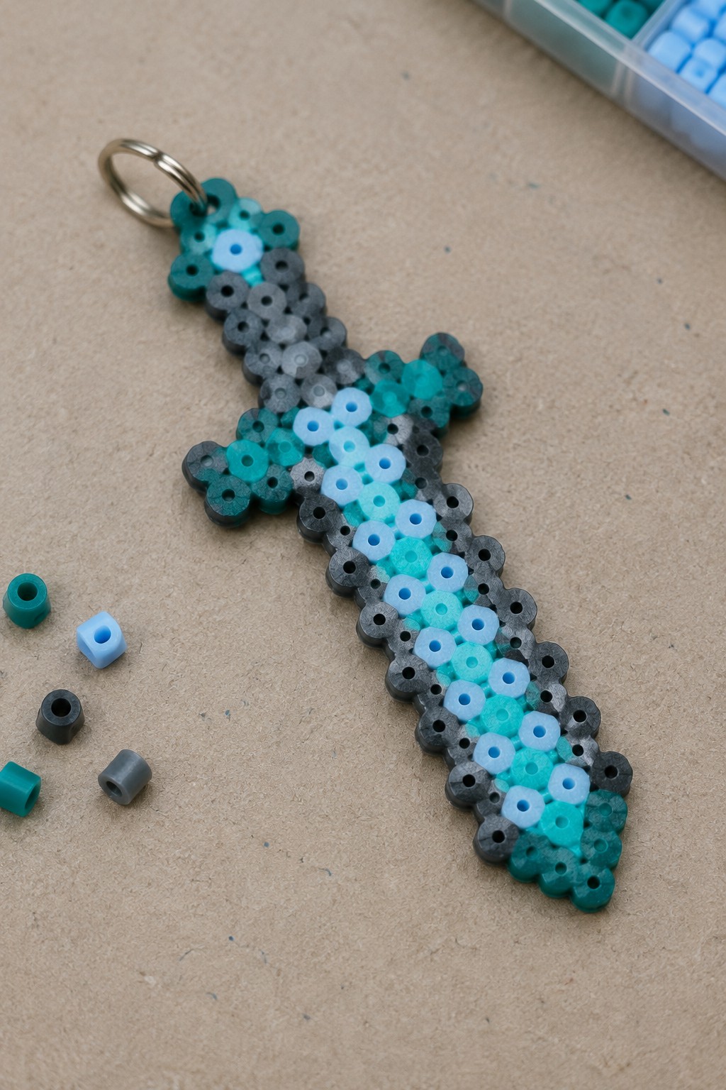 Perler bead pixel sword keychain in teal blue gray with loose beads nearby