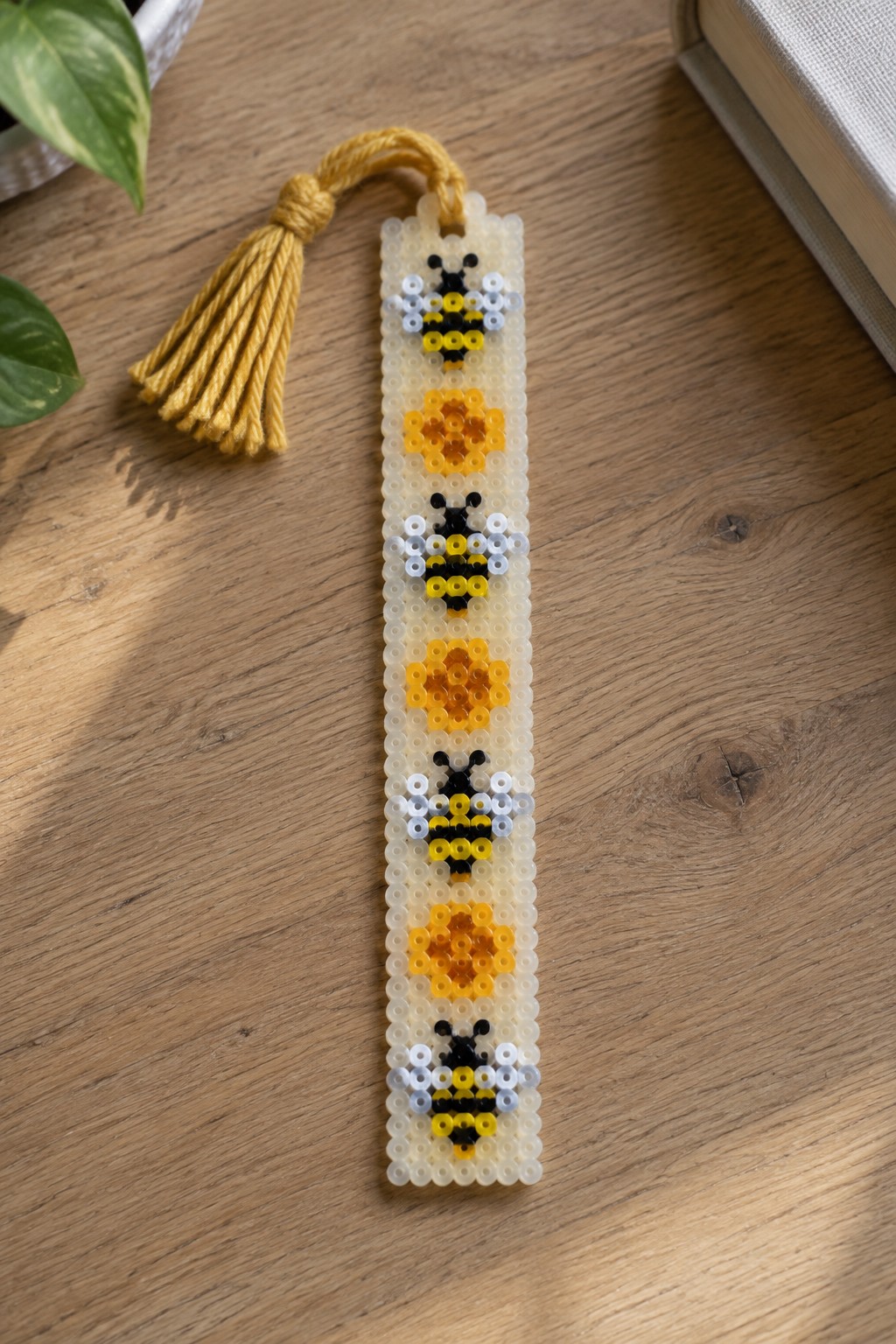 Beaded bookmark with bees, flowers, and yellow tassel on wooden surface