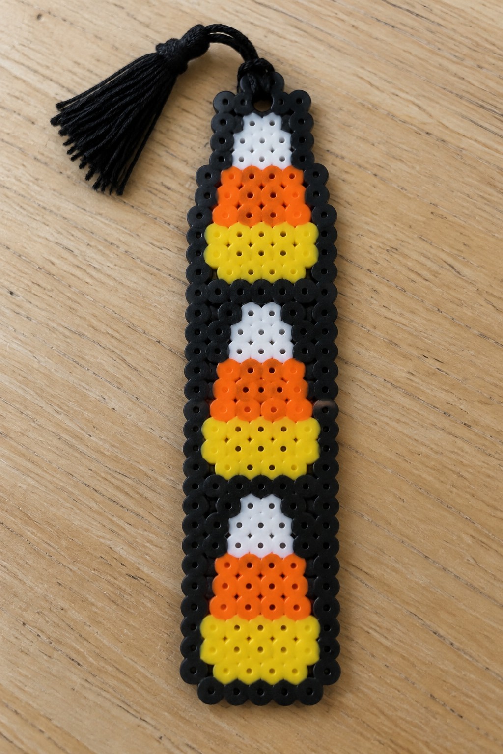 Candy corn patterned perler bead bookmark with black tassel on wood.