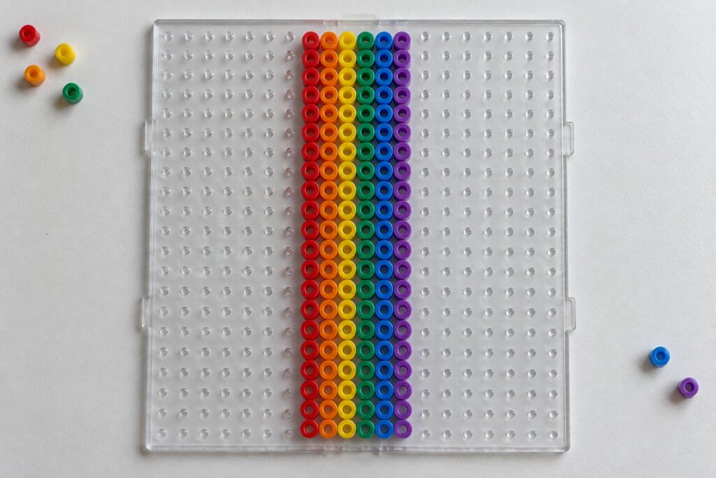 Clear pegboard with central rainbow bead pattern and loose beads scattered below