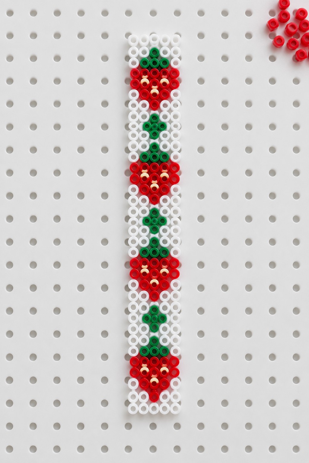 Vertical red, green, and white Perler beads forming Christmas patterns on pegboard.