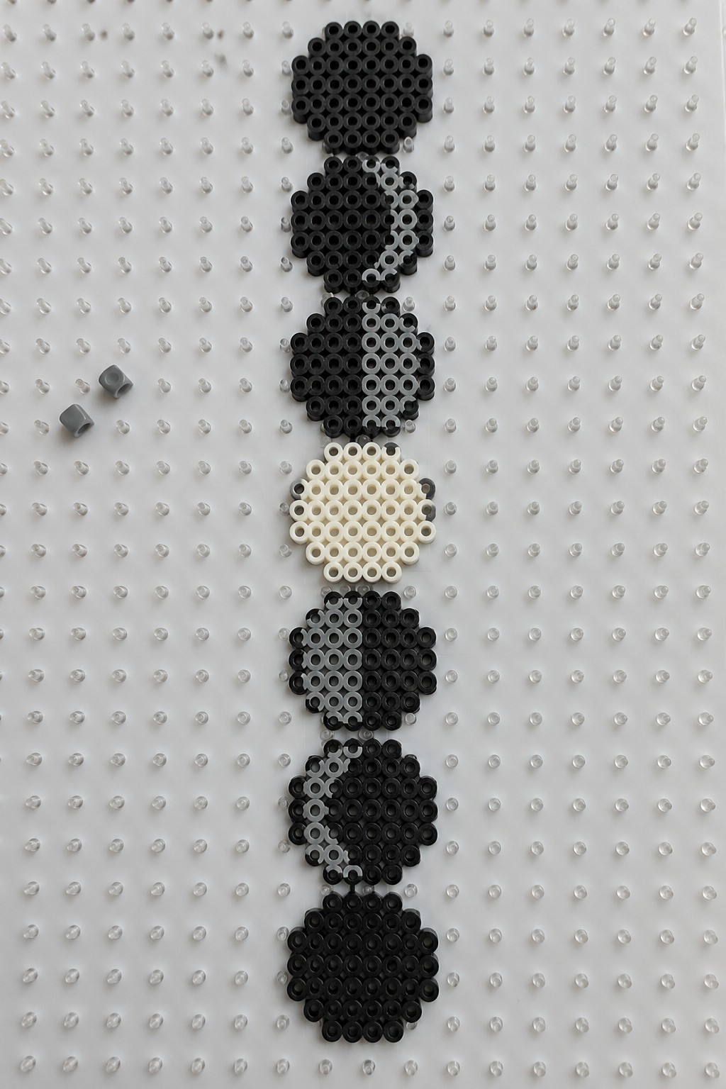Stacked black, white, and gray perler beads forming vertical patterns on pegboard