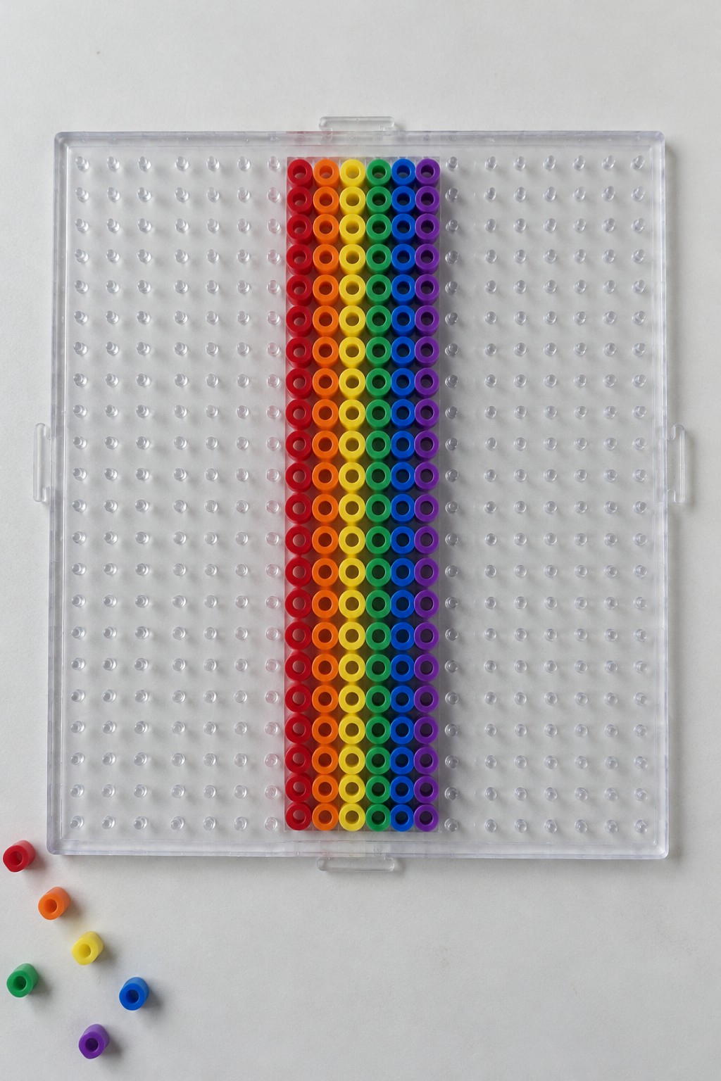 Clear pegboard with central rainbow bead pattern and loose beads scattered below