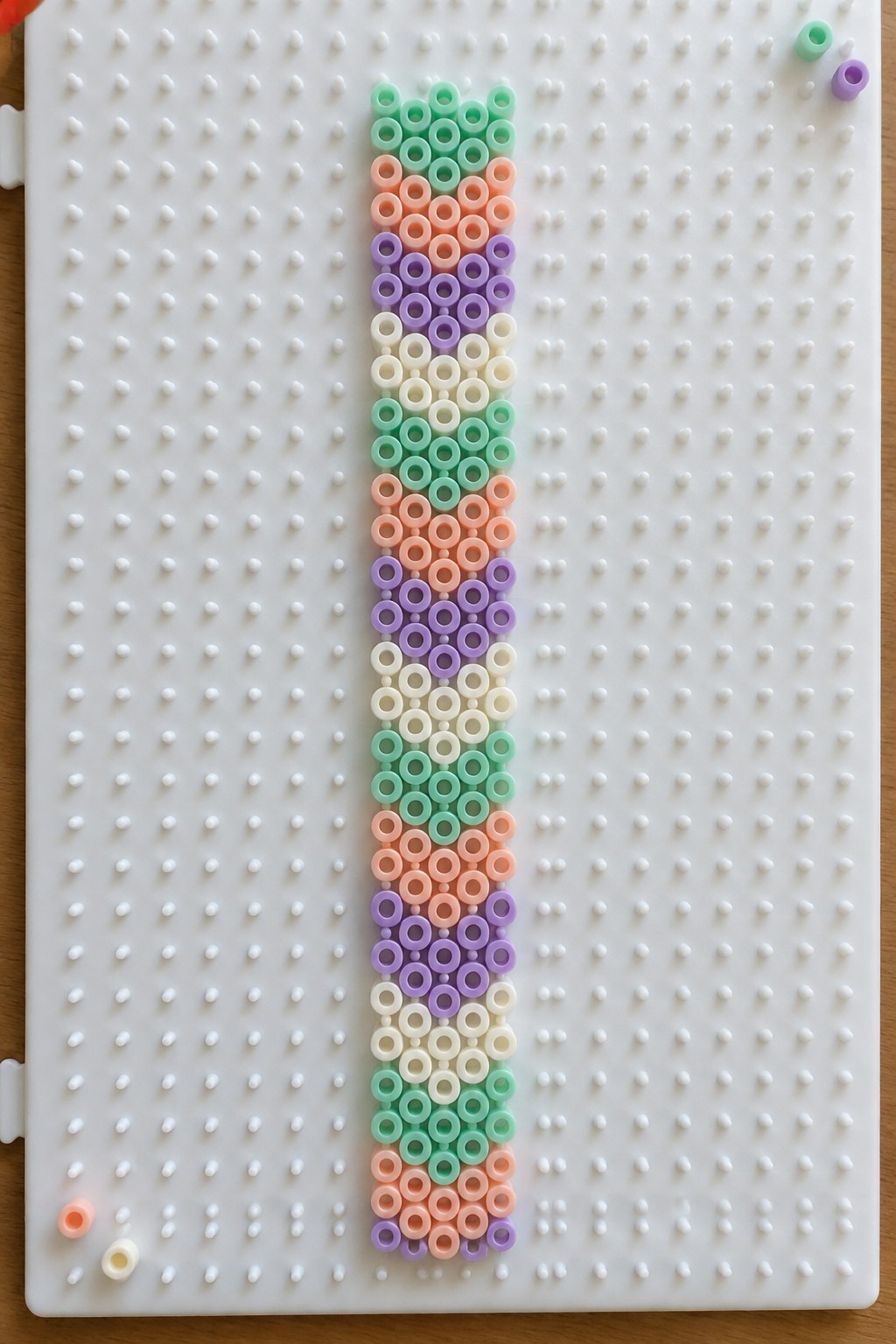 Pastel beads in mint, peach, purple and white form vertical stripes on pegboard.