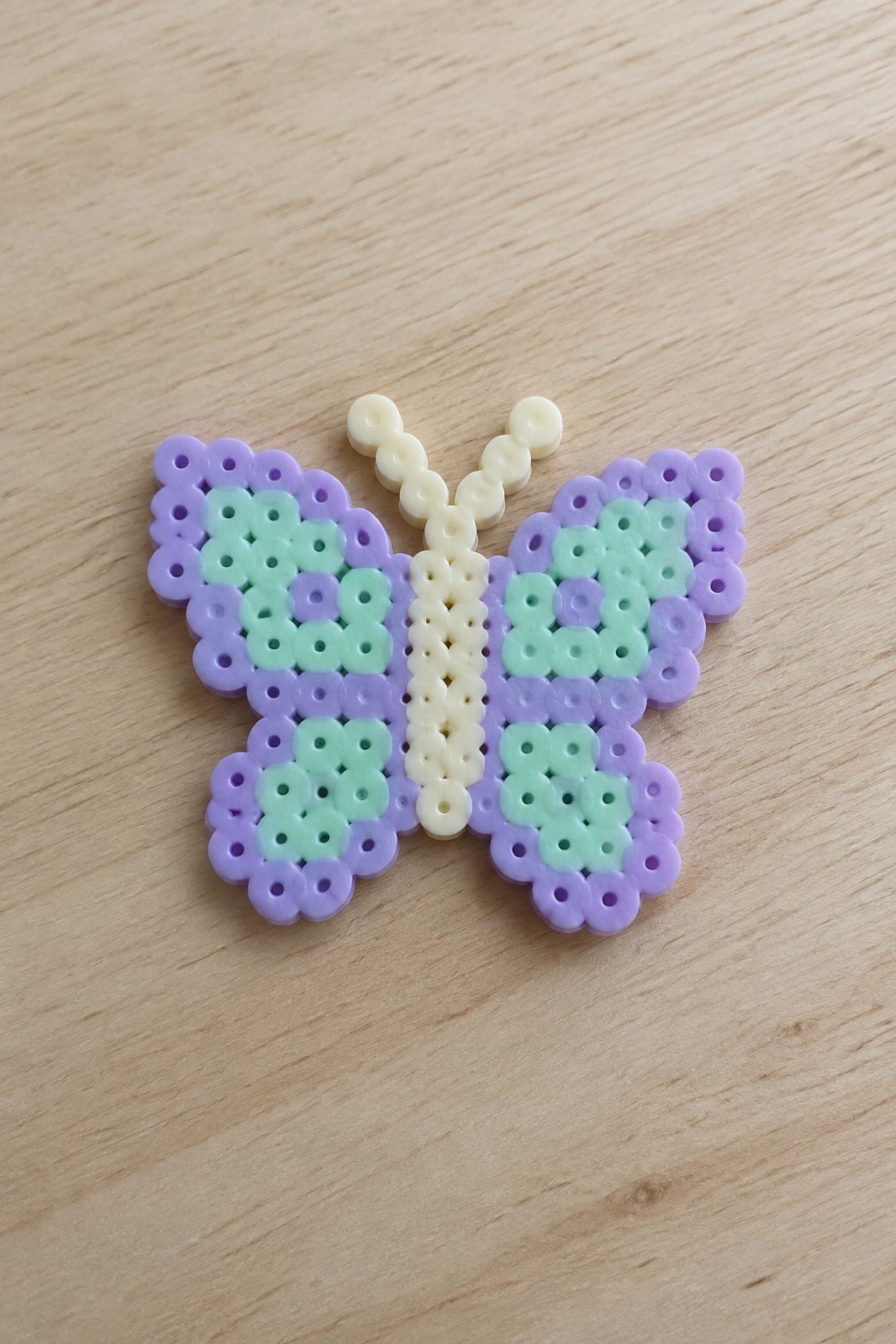 Purple and mint green perler bead butterfly with cream body on wood