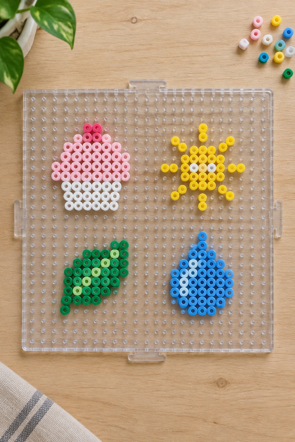Clear pegboard with pink cupcake, yellow sun, green leaf, blue droplet bead designs