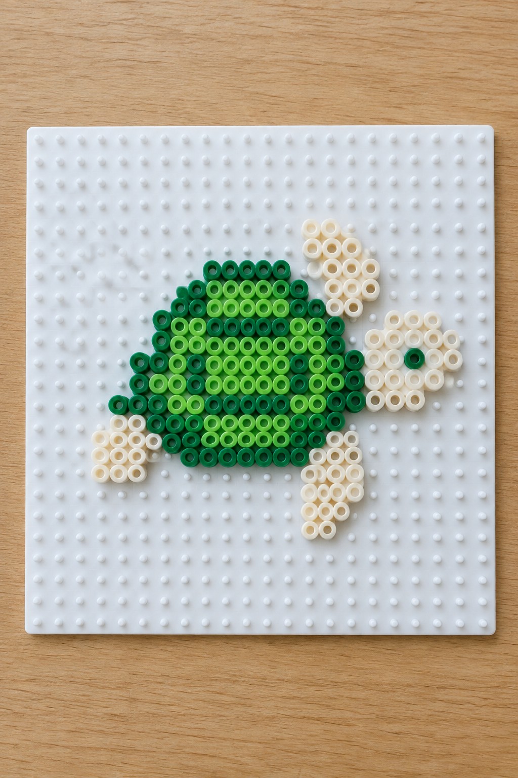 Gradient green perler bead turtle with cream limbs on white pegboard.