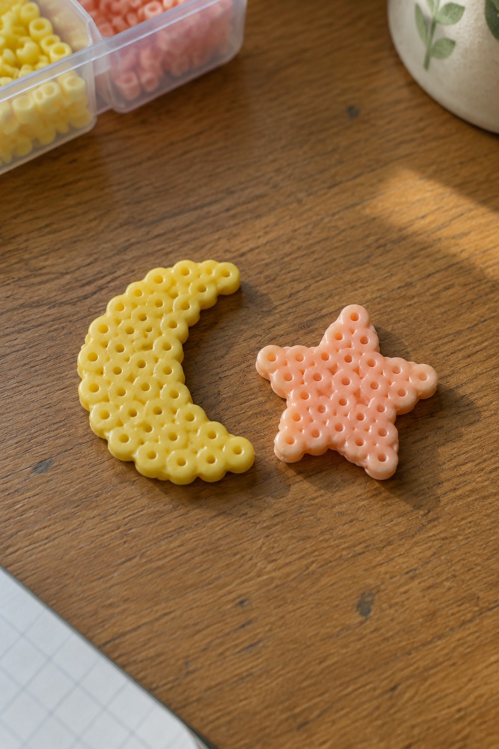 Yellow crescent moon and peach star perler beads on wooden table with containers