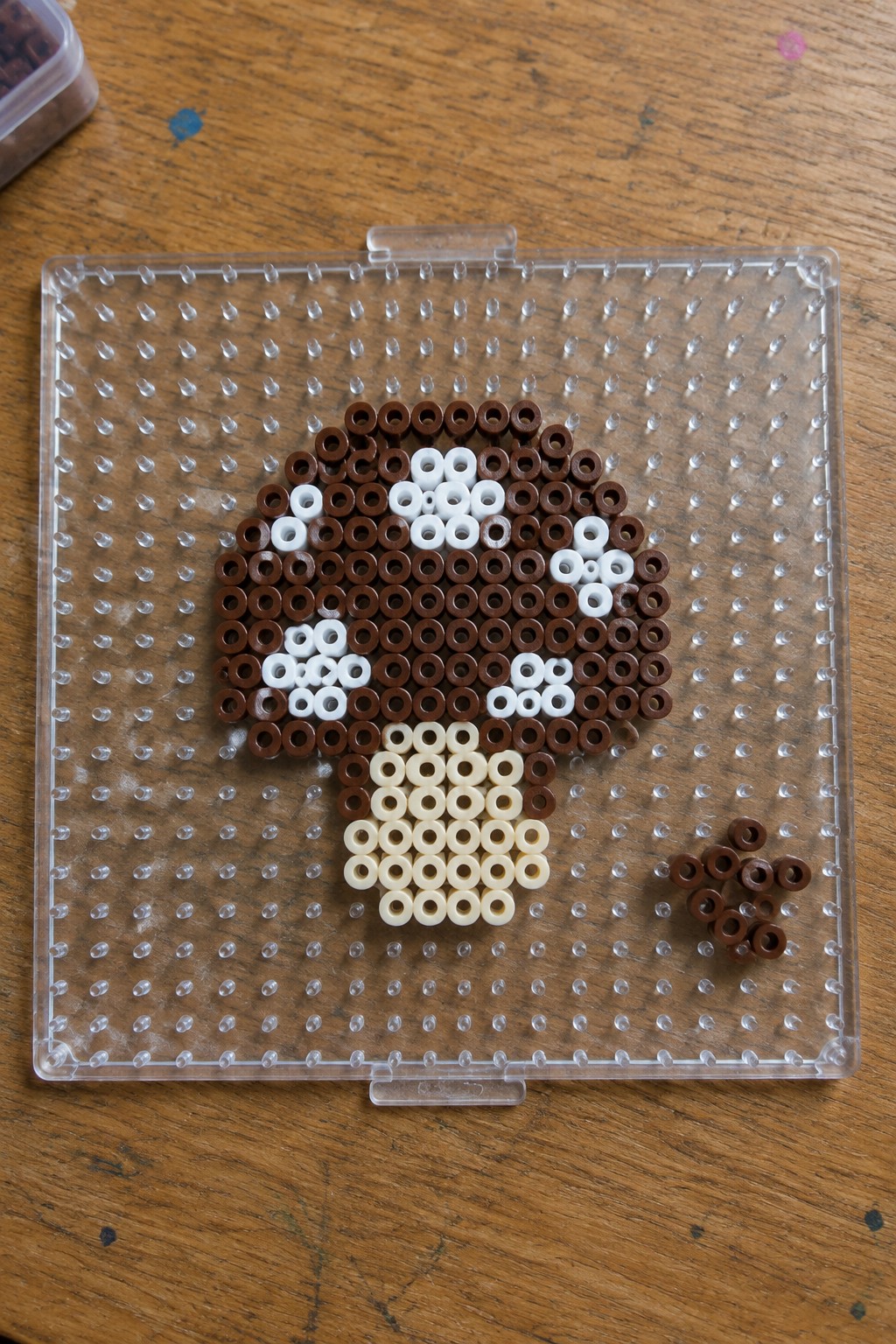 Brown and white Perler beads forming a mushroom on a clear pegboard.