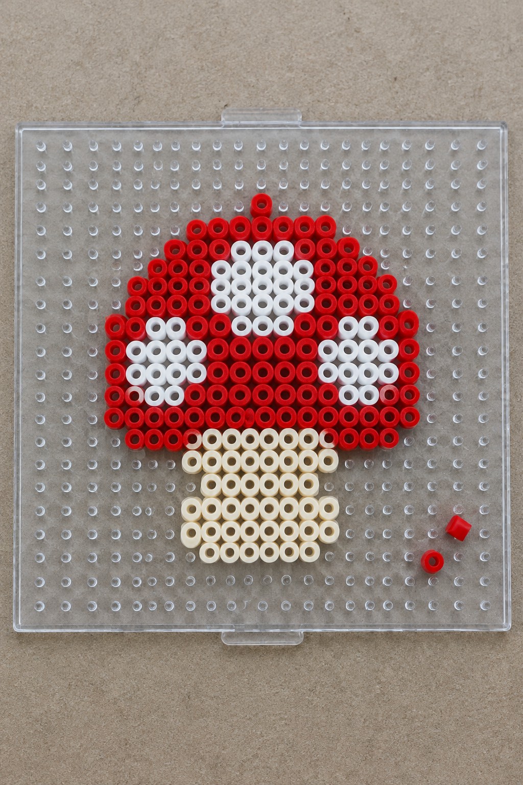 Red white and beige beads forming mushroom on clear pegboard with extras.
