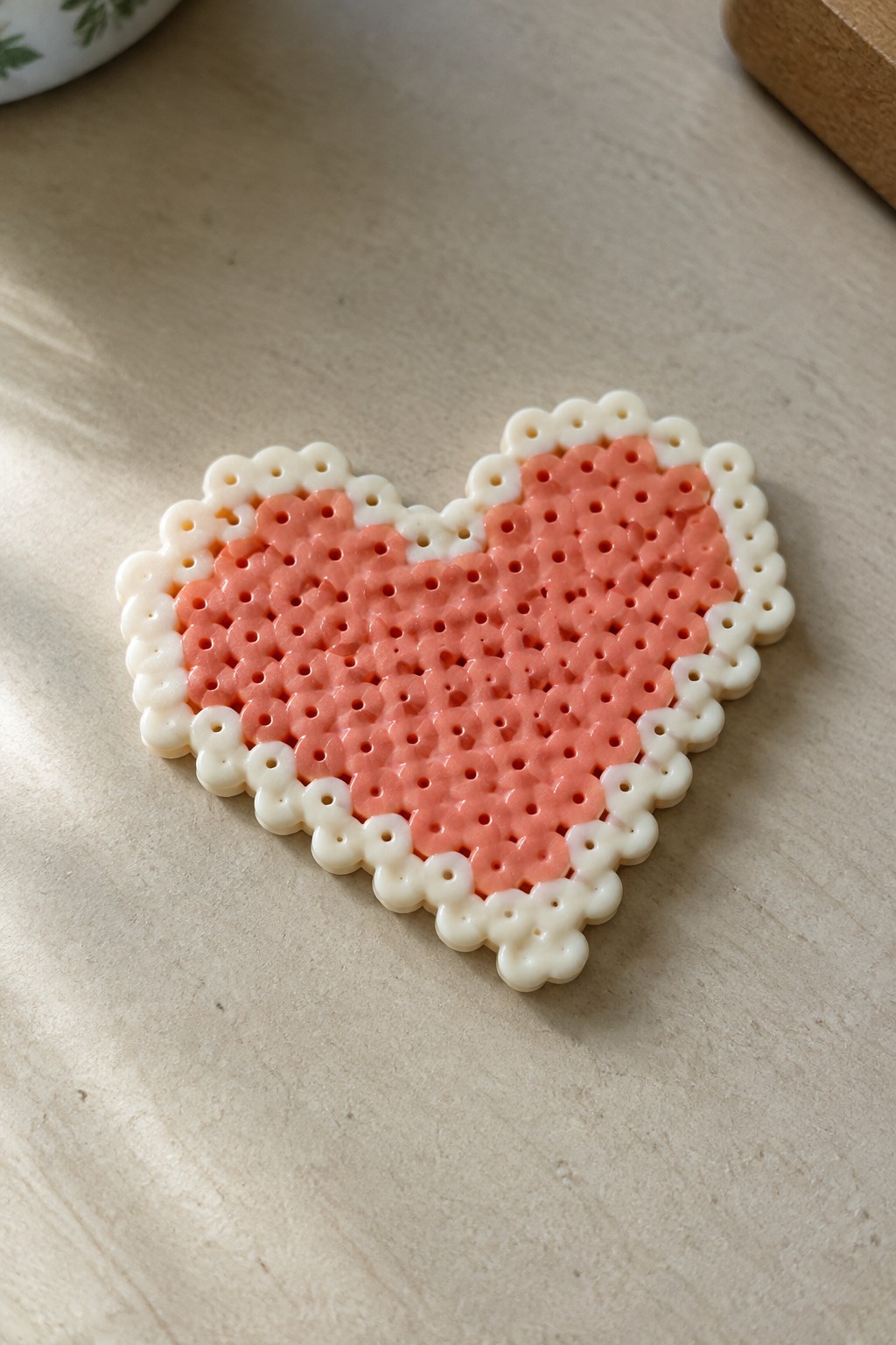 Pink and white perler bead heart with scalloped border on wooden table.