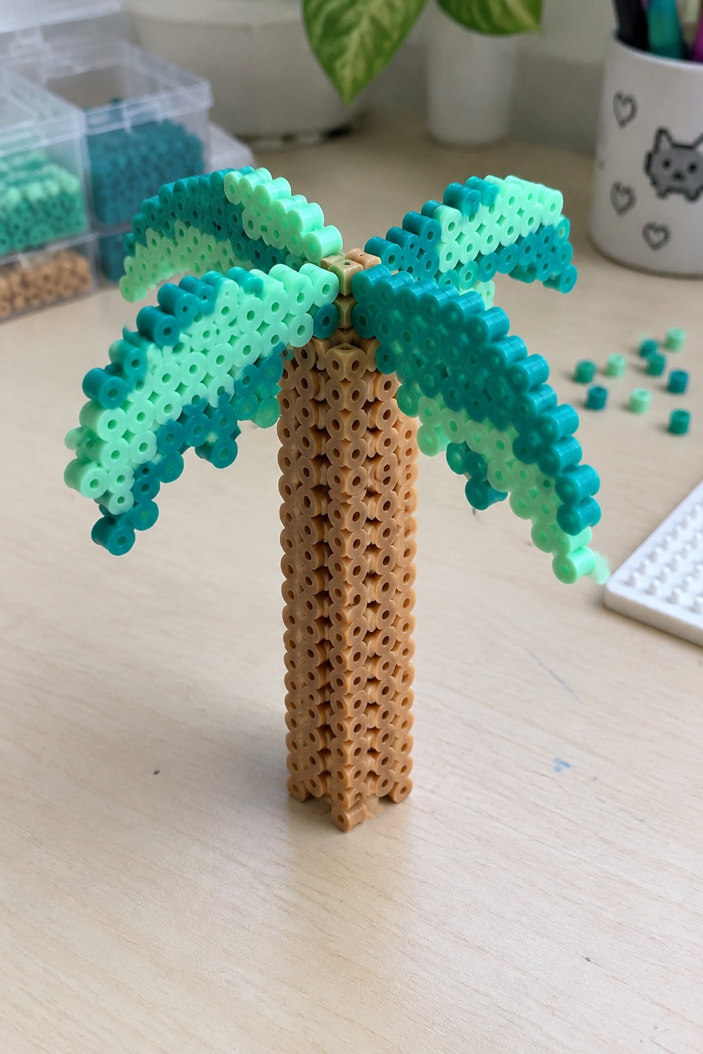 Perler bead palm tree with brown trunk and layered teal-green fronds on desk