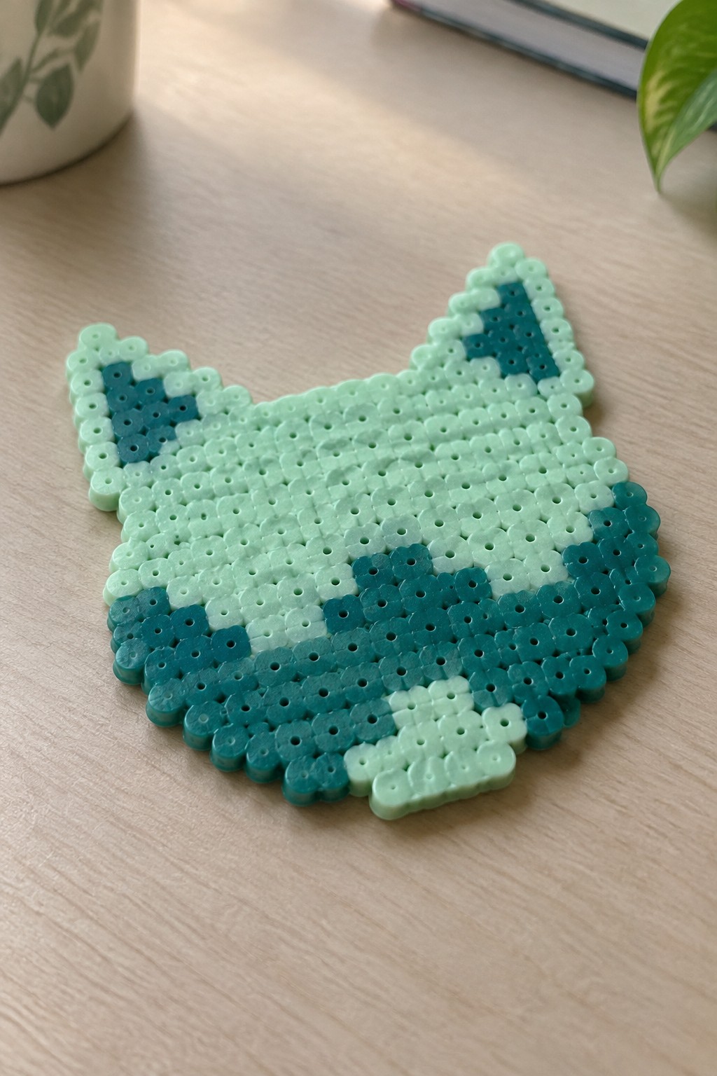 Mint green perler bead cat face with teal accents on wood