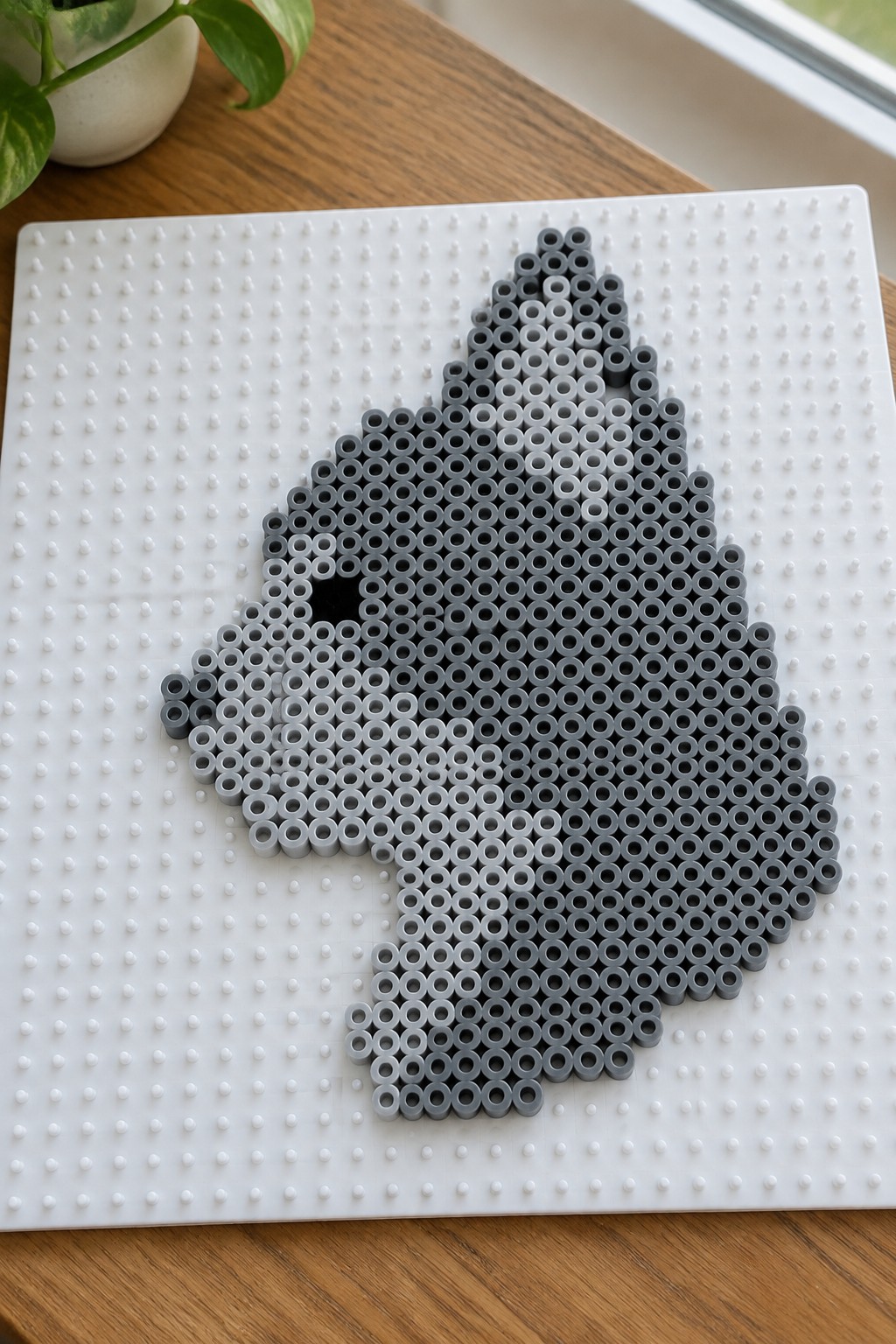 Gray Perler bead cat silhouette arranged on a white pegboard.