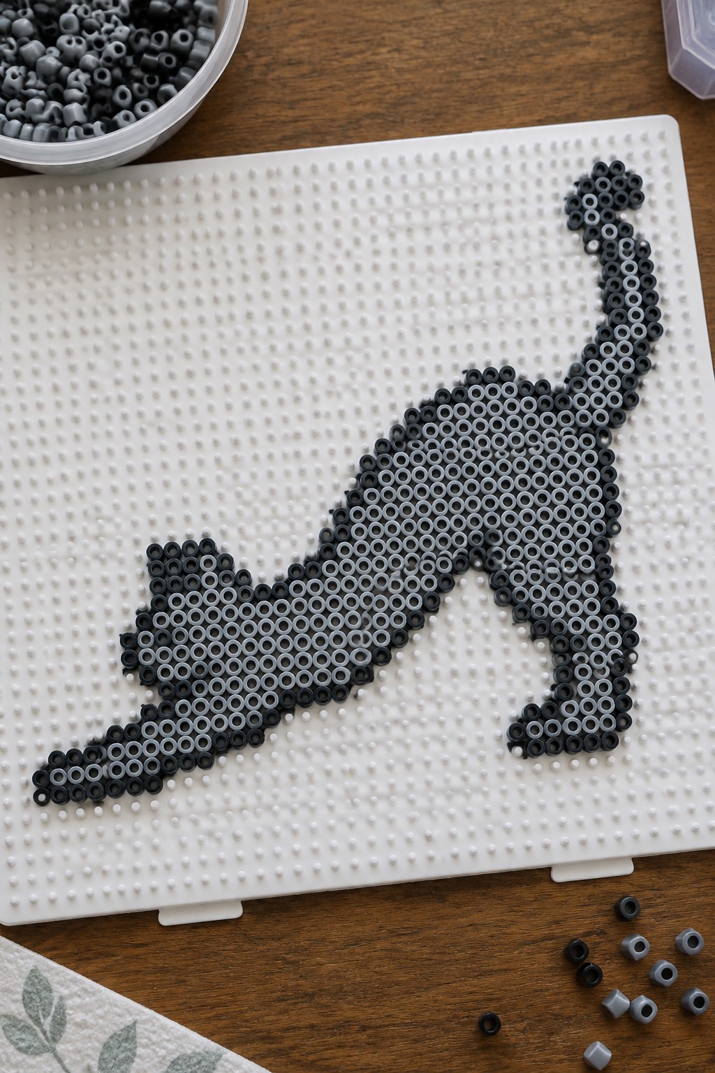 Black and gray perler beads forming a cat on white pegboard with loose beads nearby